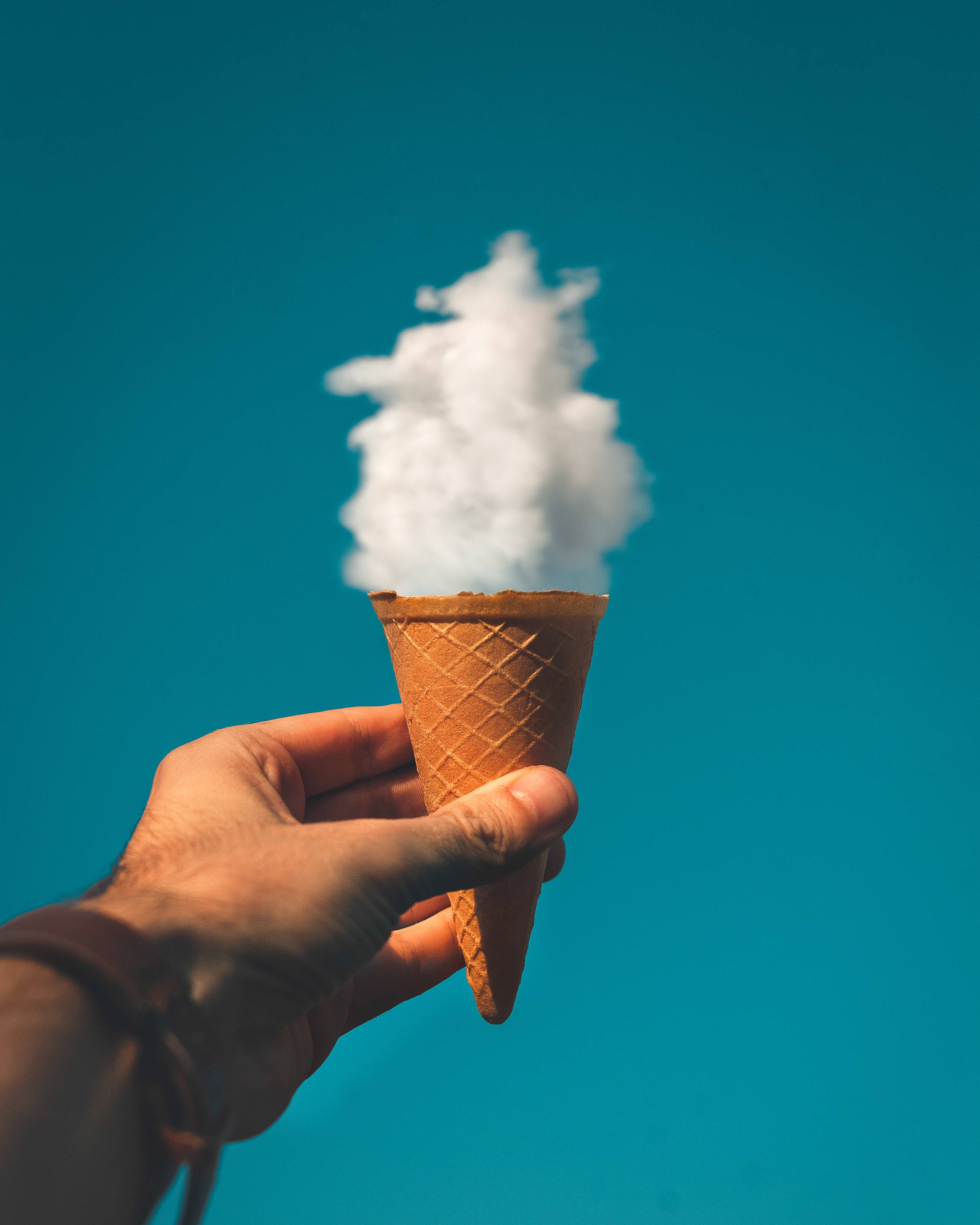Ice Cream 桌布 壁紙 — 一隻手拿著一個裝滿蓬鬆白色棉花糖的鬆餅筒，背景是充滿活力的藍綠色天空。