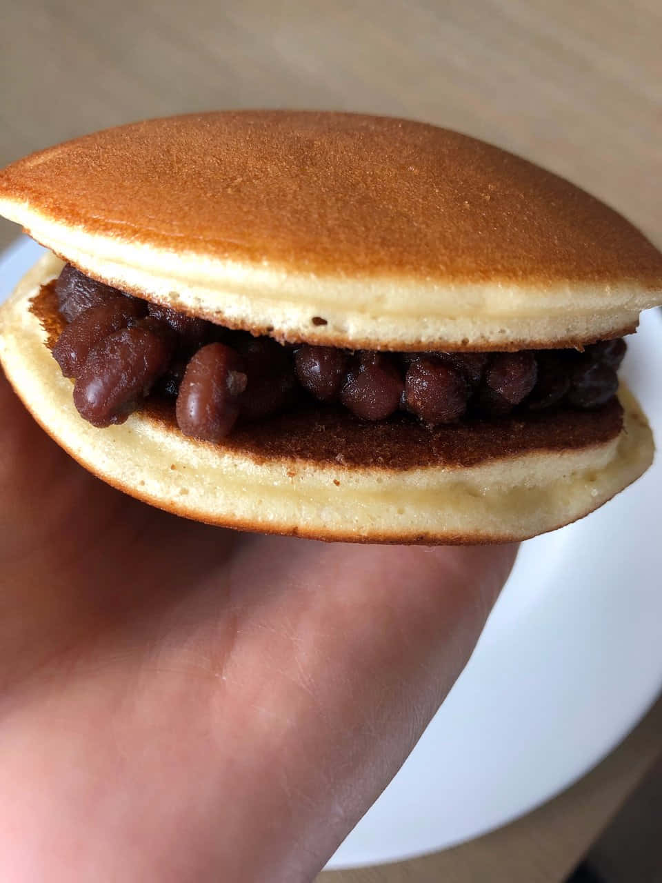 Japanese Sweets 桌布 壁紙 — 一隻手拿著一個金黃色的日本銅鑼燒，裡面填滿了甜紅豆餡。