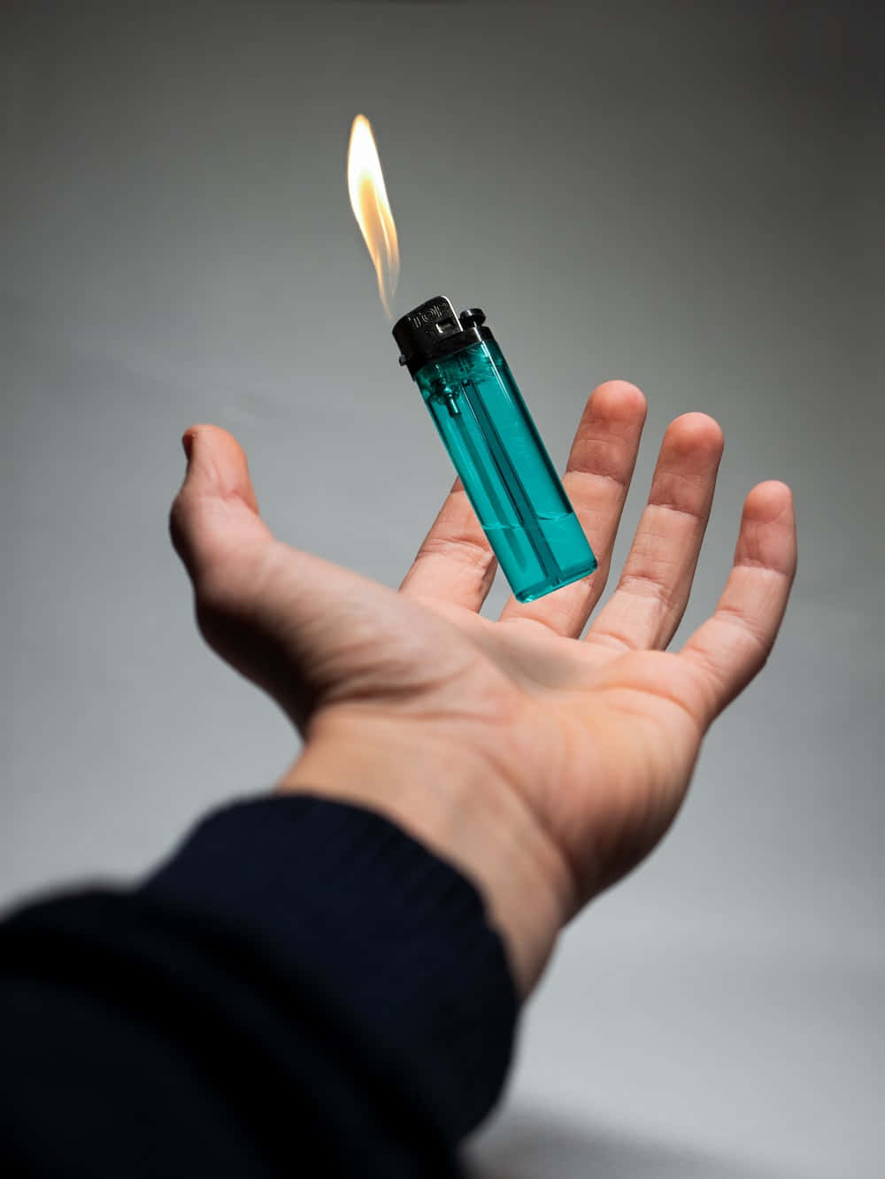 lighter 桌布 壁紙 — 一隻手拿著一個青綠色的打火機，帶有明亮的火焰，背景為中性灰色。