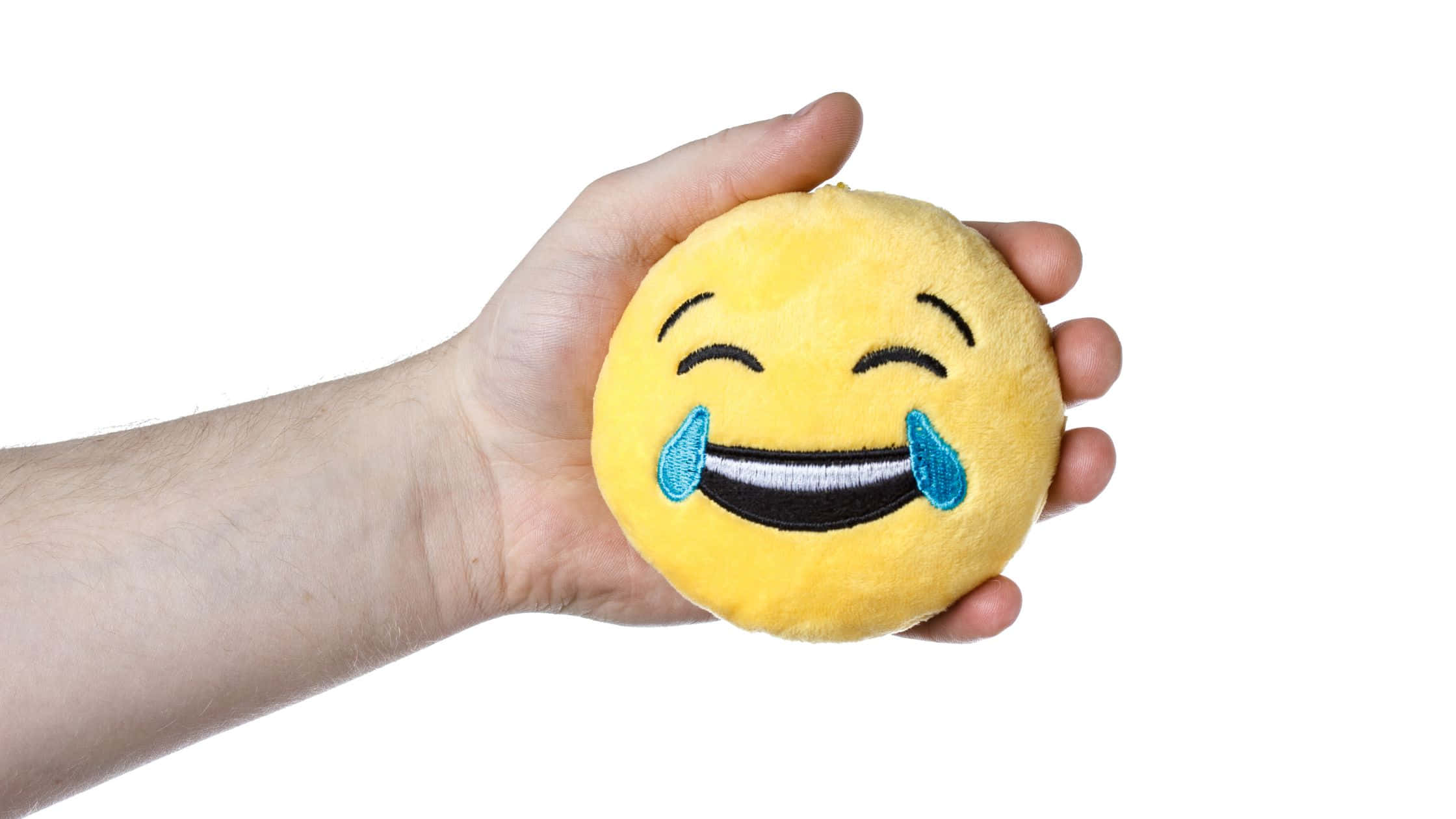 Smile 桌布 壁紙 — 一隻手拿著一個黃色毛絨笑臉表情枕頭，帶有藍色眼淚，背景為白色。