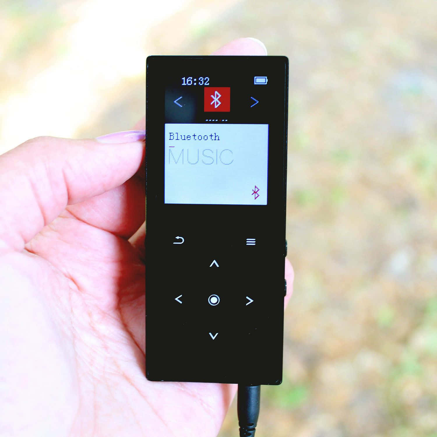 Music Player 桌布 壁紙 — 一隻手拿著一個黑色便攜式音樂播放器，在模糊的戶外背景下顯示藍牙音樂連接。