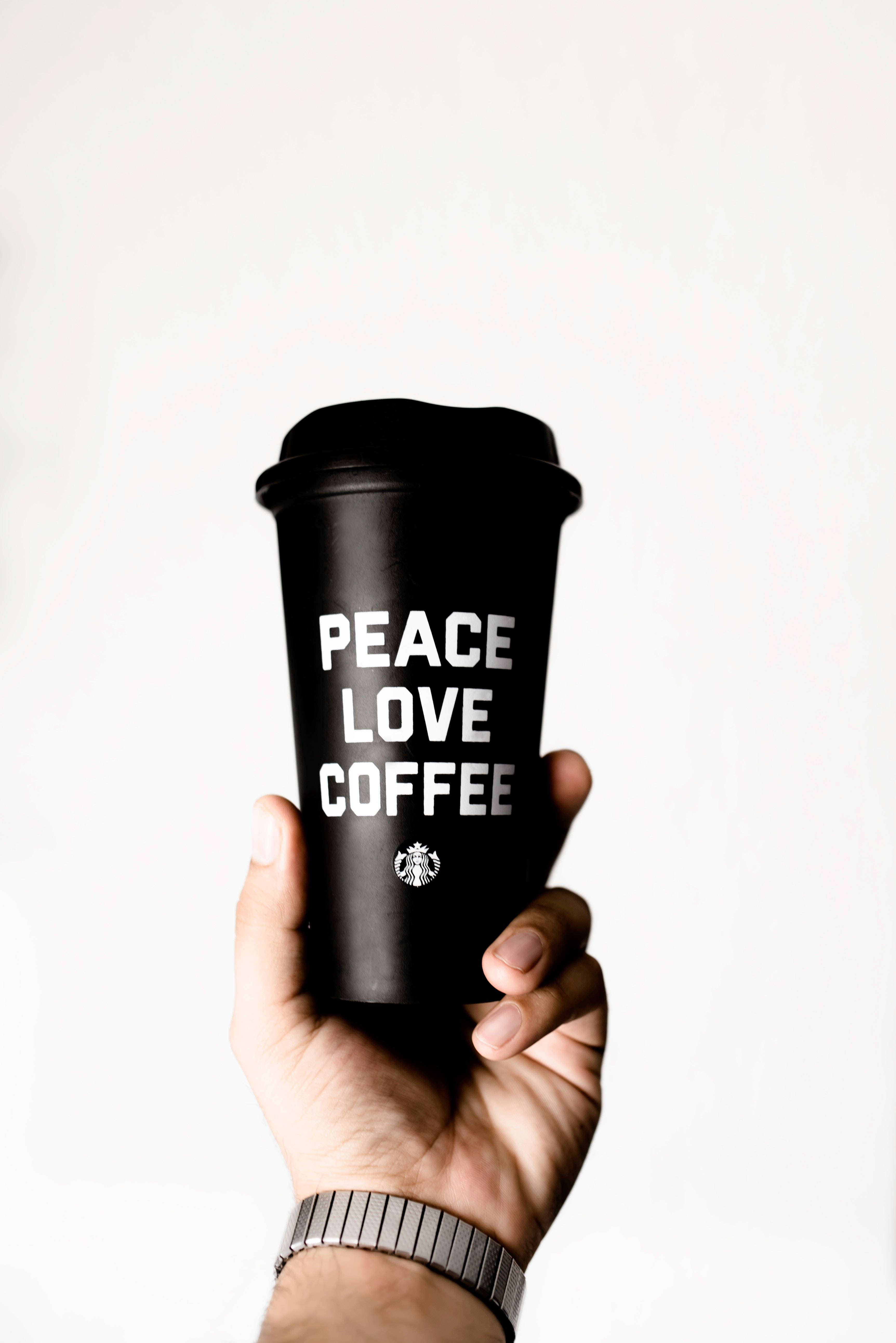 和平 桌布 壁紙 — 一隻手拿著一個黑色的Starbucks旅行杯，杯上有白色文字peace love coffee，背景為純白色。