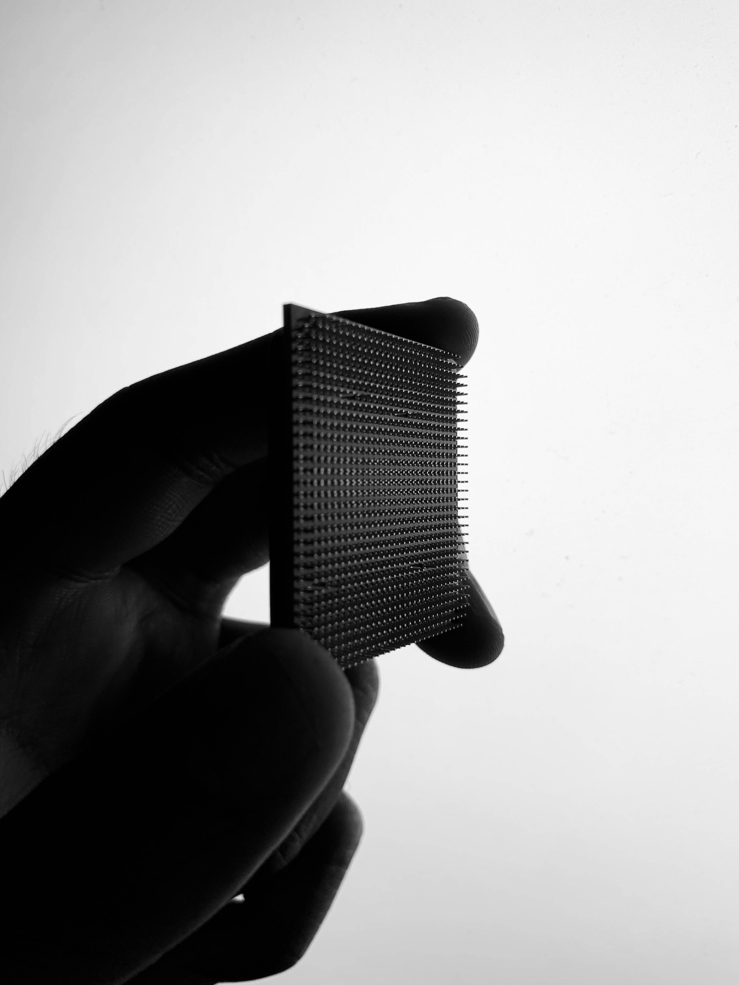 Processor 桌布 壁紙 — 一隻手拿著一個黑色長方形物體，上面有精細尖刺的網格，背景是純白色。