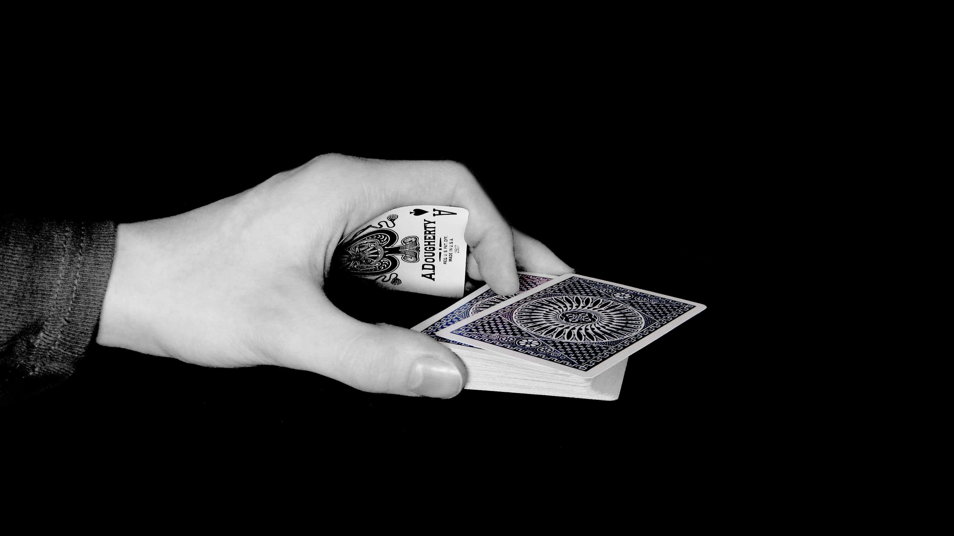 Poker 桌布 壁紙 — 一隻手拿著一副撲克牌，背景是純黑色，黑桃Ace露出來。