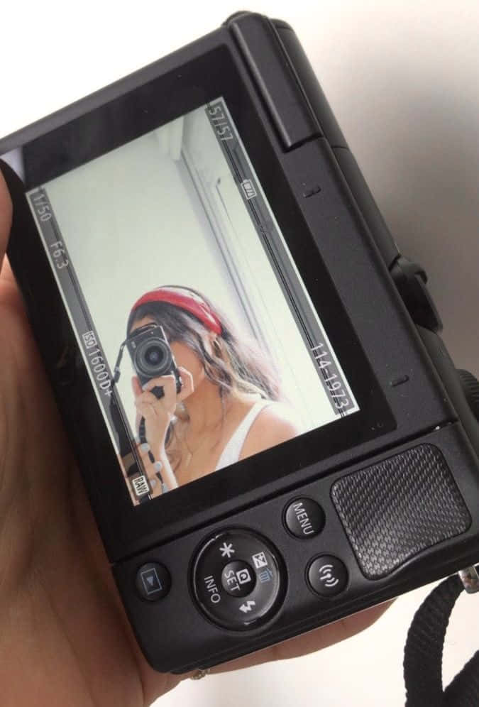 Holding Camera 桌布 壁紙 — 一隻手拿著一台黑色數位相機，螢幕上顯示一位戴著紅色頭帶的女子的自拍照。