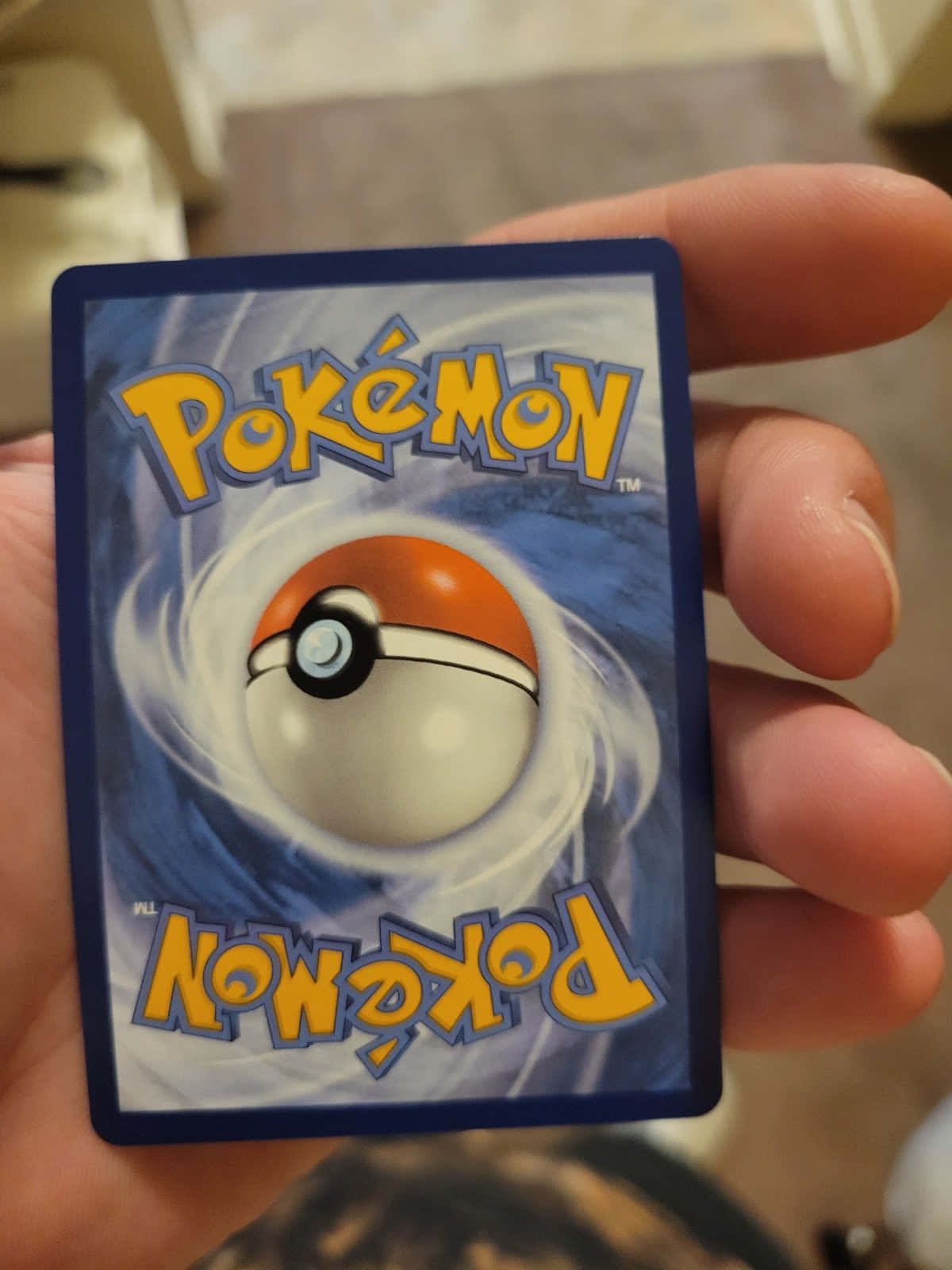 Pokemon Card 桌布 壁紙 — 一隻手拿著一張寶可夢集換式卡牌，卡牌上有旋轉的精靈球標誌，背景為藍色。