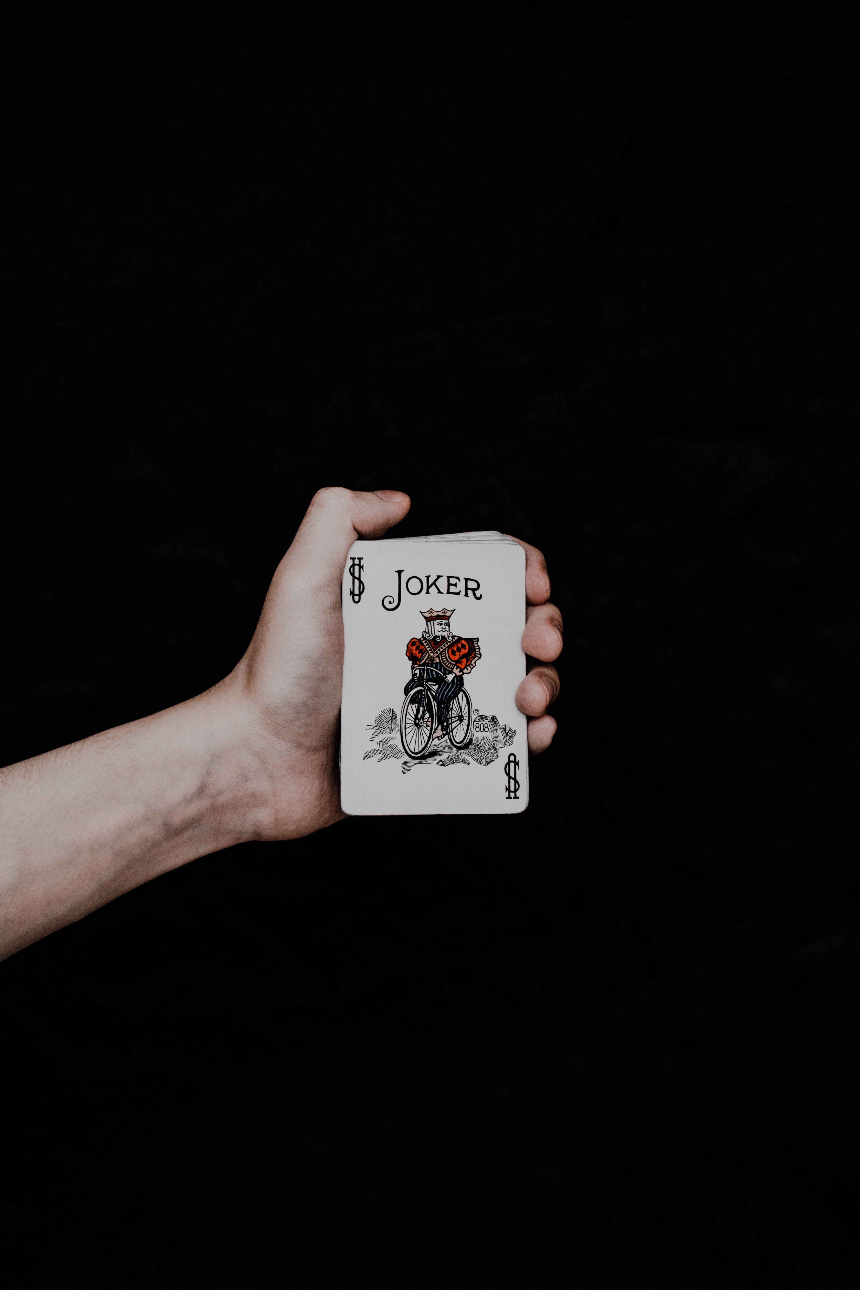 小丑 桌布 壁紙 — 一隻手拿著一張小丑撲克牌，背景是黑色紋理。