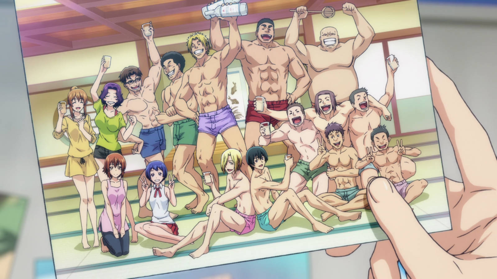 Grand Blue 桌布 壁紙 — 一隻手拿著一張照片，照片中一群活潑的動漫角色穿著泳衣在傳統日本澡堂裡快樂地擺姿勢。