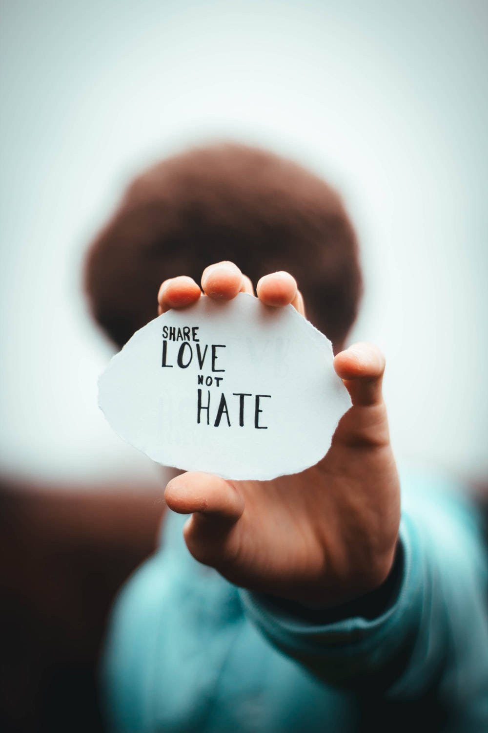hate 桌布 壁紙 — 一隻手拿著一張白紙，上面有粗體黑色文字寫著share love not hate，背景柔和模糊。