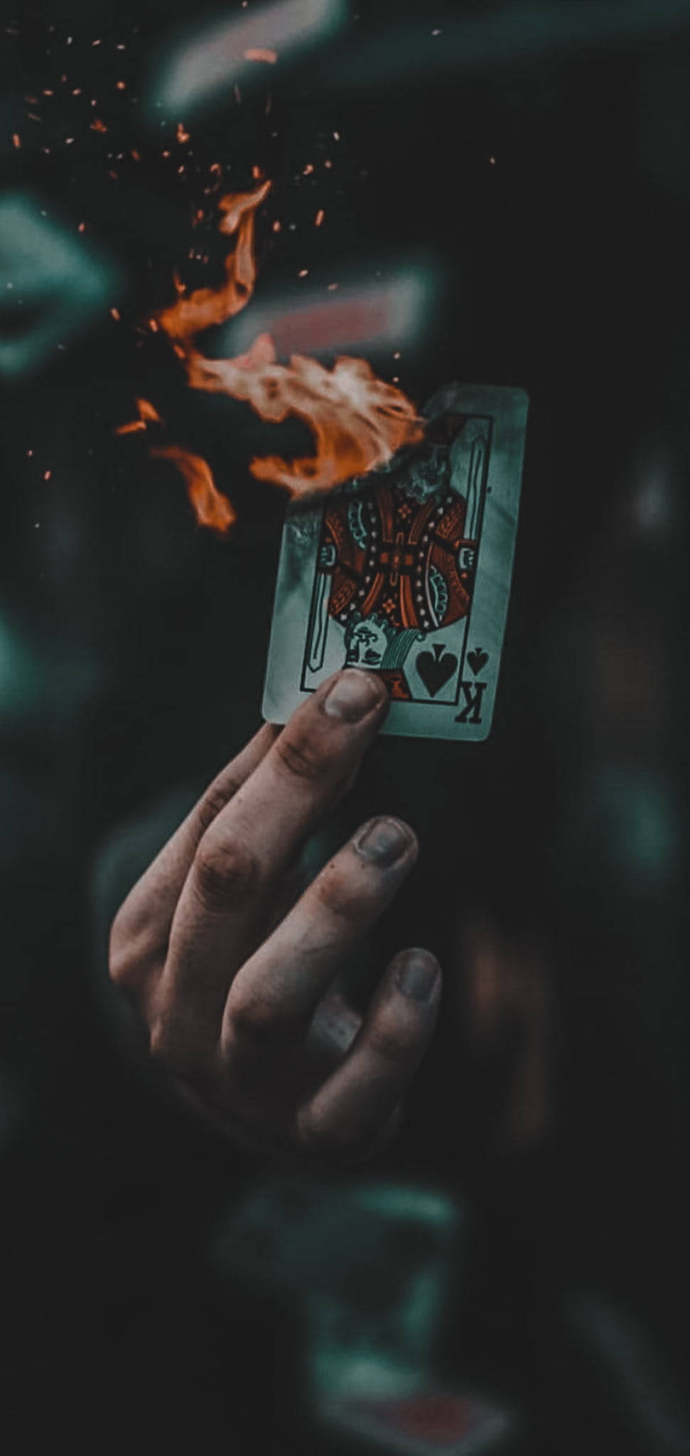 Single 桌布 壁紙 — 一隻手拿著一張紅心K撲克牌，它在深藍綠色背景上燃燒著橙色火焰和火花。