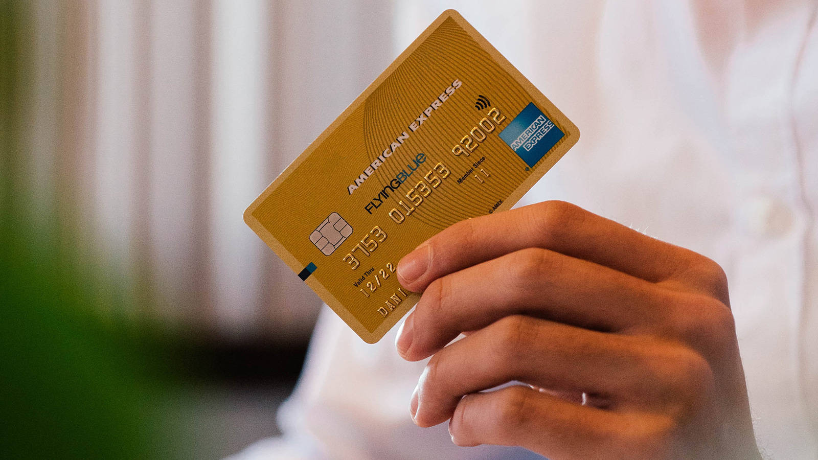 Credit Card 桌布 壁紙 — 一隻手拿著一張金色美國運通卡，晶片和到期日清晰可見，背景柔和模糊。