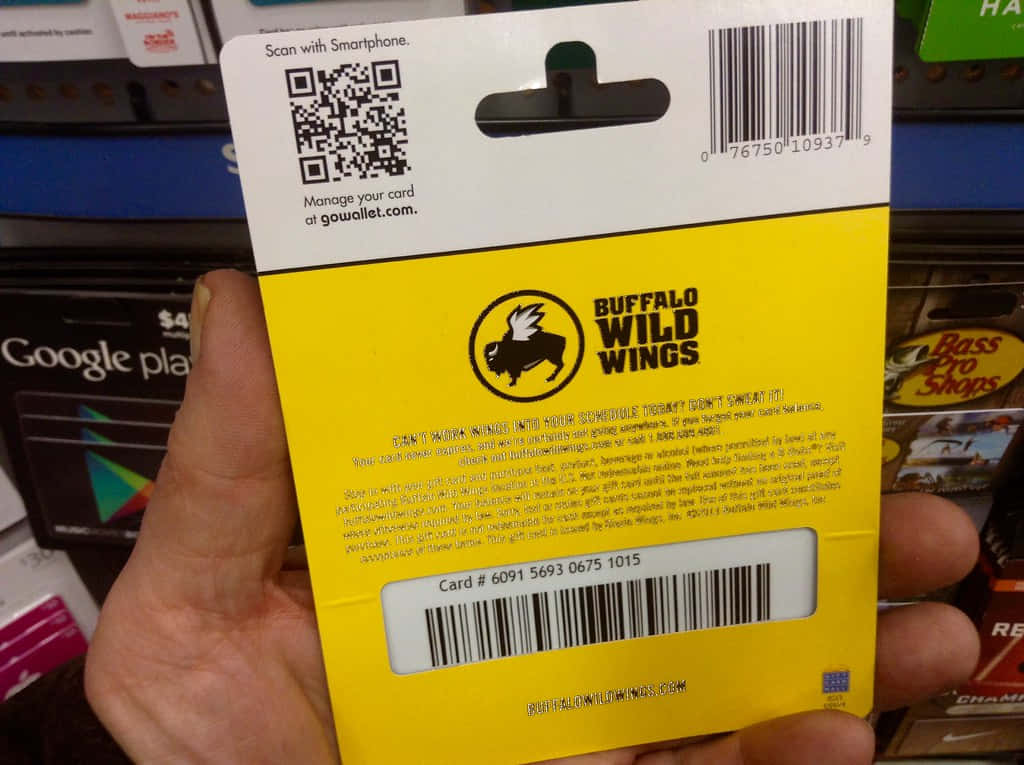 水牛城辣雞翅 桌布 壁紙 — 一隻手拿著一張黃色Buffalo Wild Wings禮品卡背面，上面有條碼和標誌，背景是模糊的商店貨架。