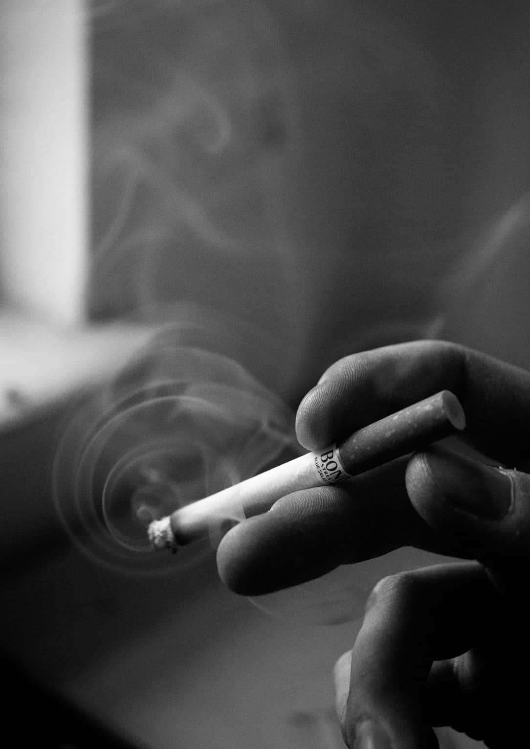 黑白 桌布 壁紙 — 一隻手拿著一支冒煙的香煙，煙霧繚繞，背景是模糊的黑白單色。
