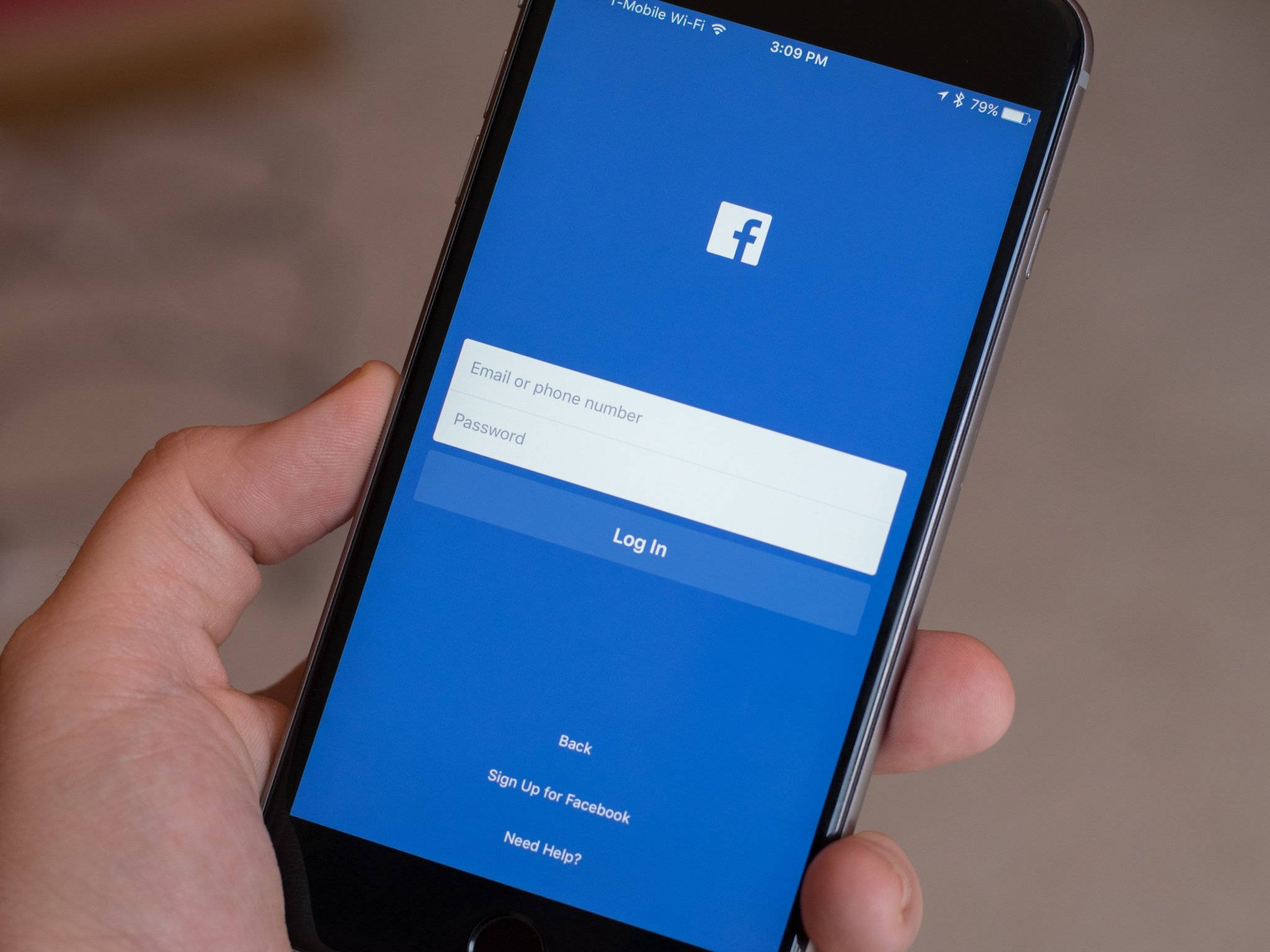 Facebook Login 桌布 壁紙 — 一隻手拿著一支智慧型手機，顯示Facebook登入畫面，背景為藍色，輸入欄位為白色。