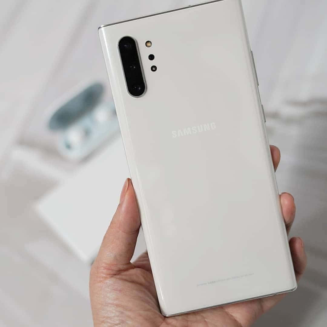 Note 10 桌布 壁紙 — 一隻手拿著一支白色Samsung智慧型手機，背面光滑，垂直相機模組，背景柔和模糊。