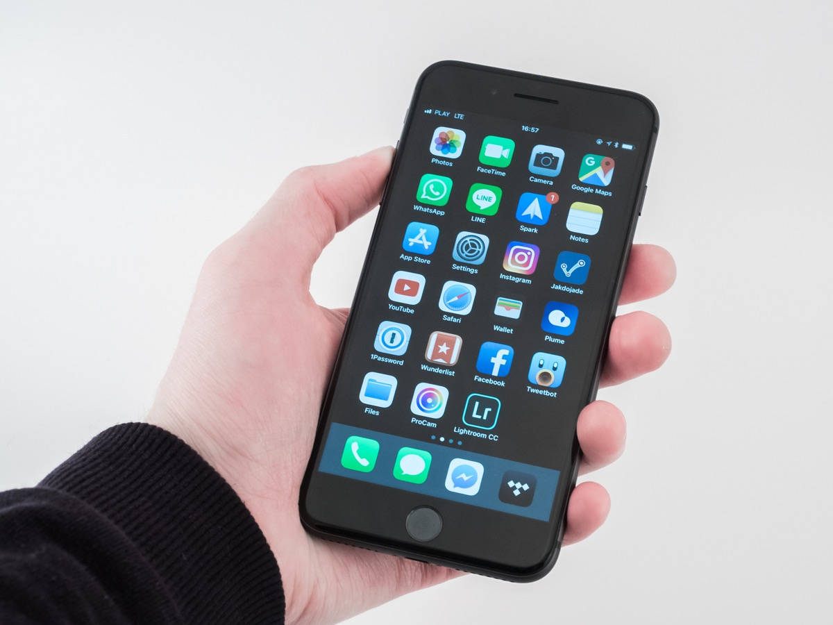 iPhone 8 桌布 壁紙 — 一隻手拿著一支黑色智慧型手機，螢幕上顯示彩色應用程式圖示的網格，背景為純白色。