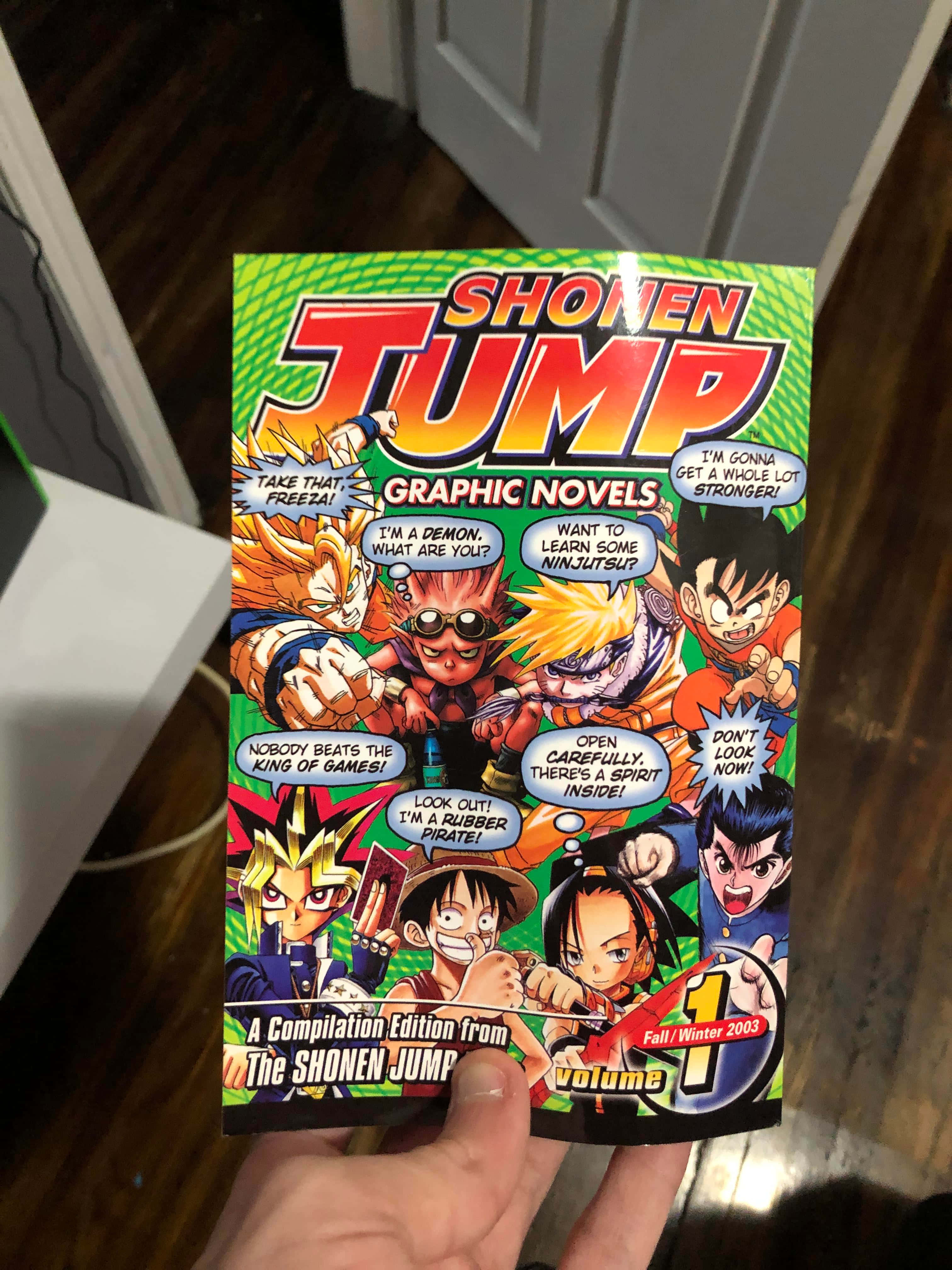 Shonen Jump 桌布 壁紙 — 一隻手拿著一本充滿活力的少年Jump圖像小說封面，上面有動漫角色擺出動態動作姿勢並附有對話氣泡。