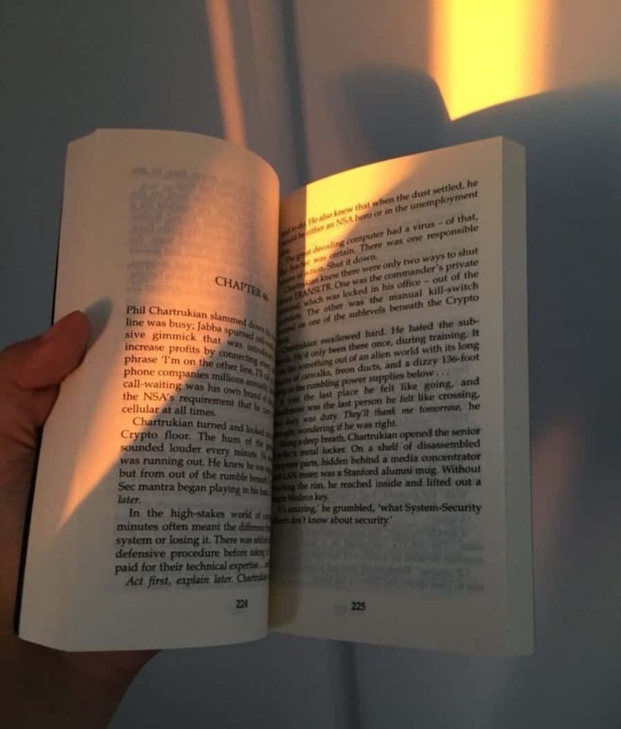 Open Book 桌布 壁紙 — 一隻手拿著一本打開的平裝小說，在溫暖的環境燈光下可見文字和頁碼。