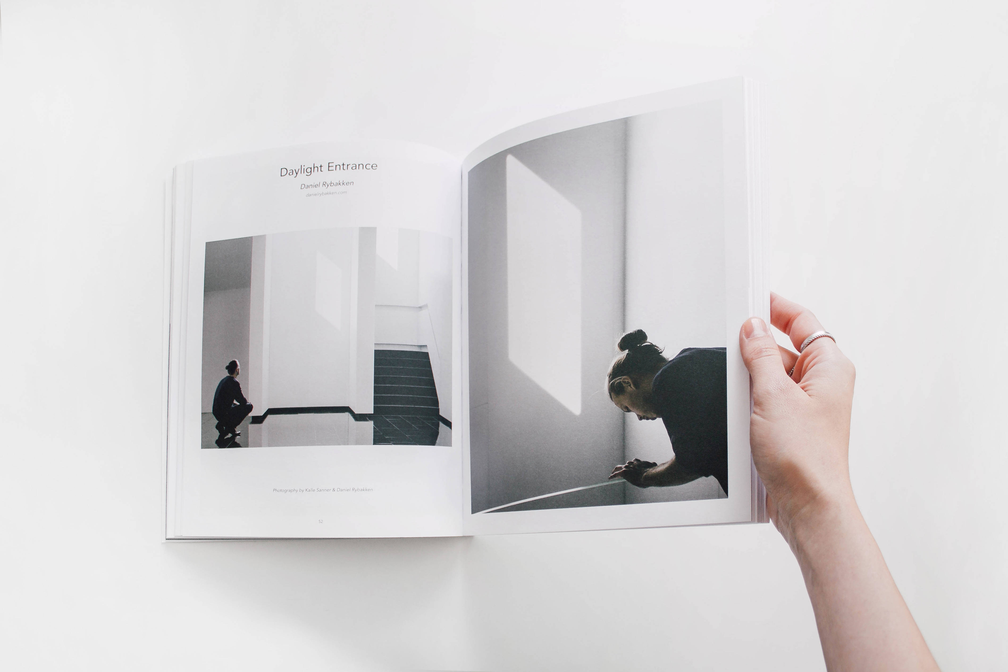 Magazine 桌布 壁紙 — 一隻手拿著一本打開的書，展示兩張黑白建築照片，呈現極簡主義室內設計和強烈的幾何光線圖案。