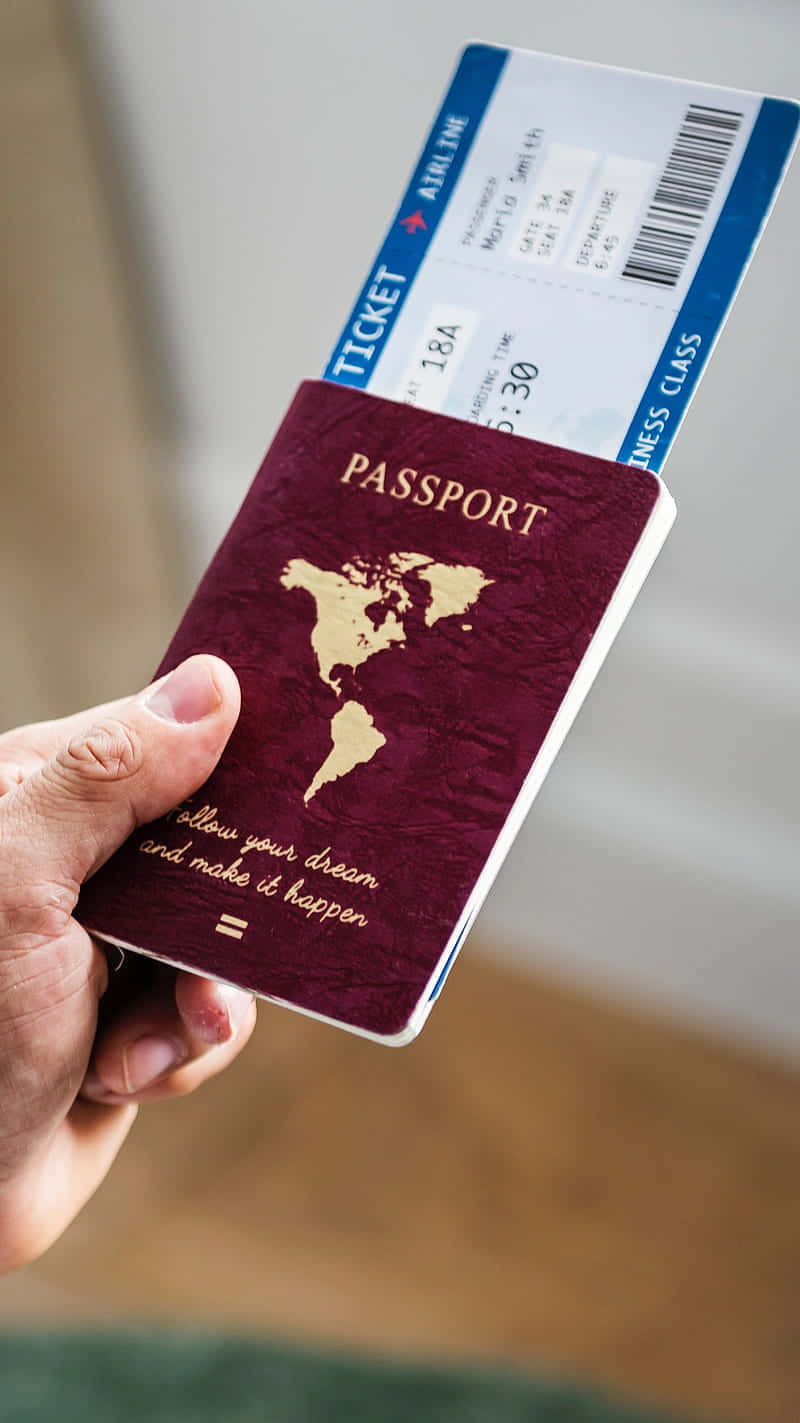Passport 桌布 壁紙 — 一隻手拿著一本栗色護照，上面有金色世界地圖和勵志語句，旁邊還有一張商務艙機票。