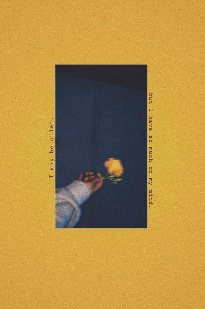 Aesthetic Mood 桌布 壁紙 — 一隻手拿著一朵黃玫瑰，背景是深藍色，由溫暖的黃色牆壁框住，帶有詩意的文字。