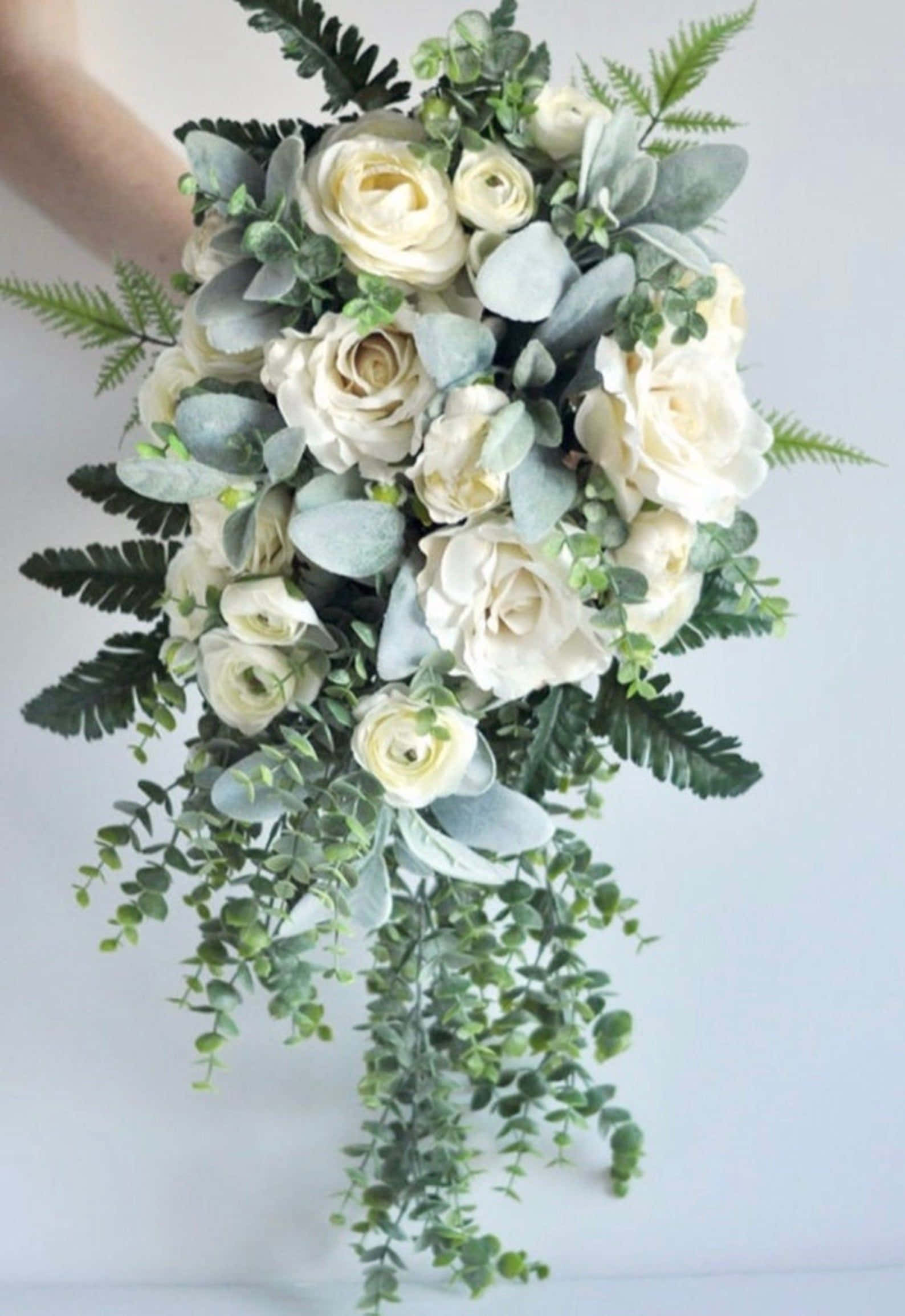 Bouquet 桌布 壁紙 — 一隻手拿著一束奶油白玫瑰和茂盛綠葉組成的瀑布式花束，背景是柔和的白色。