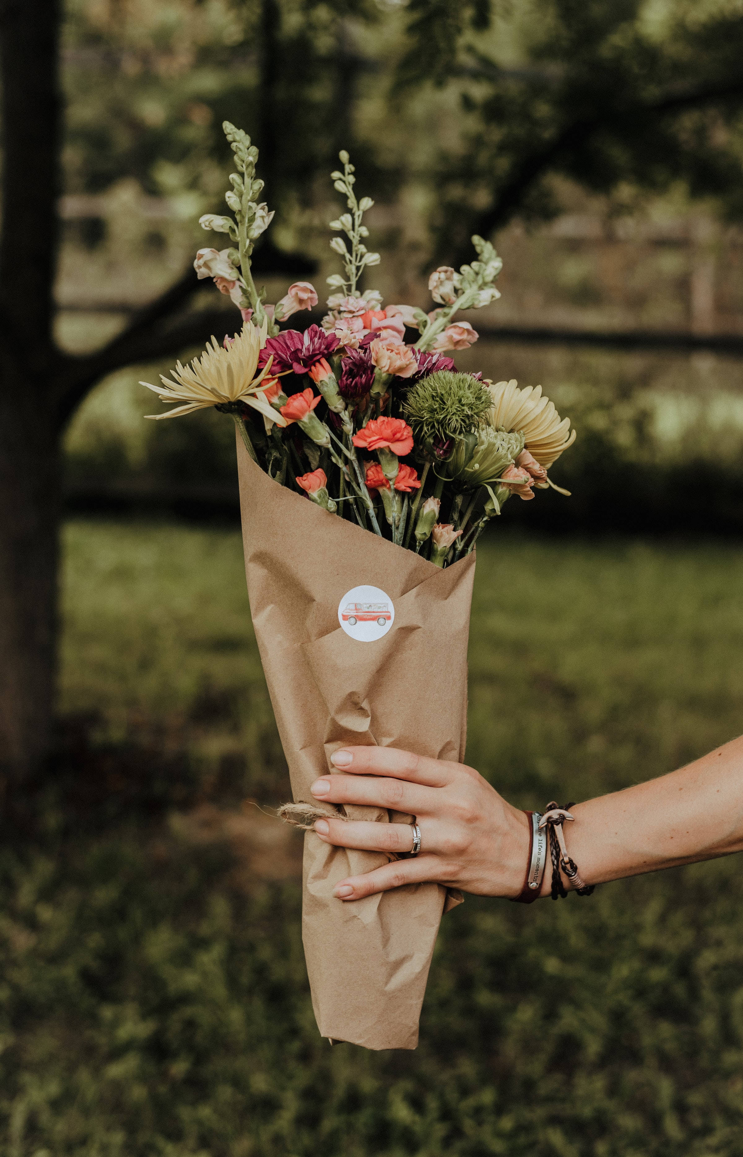 Bouquet 桌布 壁紙 — 一隻手拿著一束用牛皮紙包裹的鮮豔雜花，背景是柔和模糊的綠色花園。