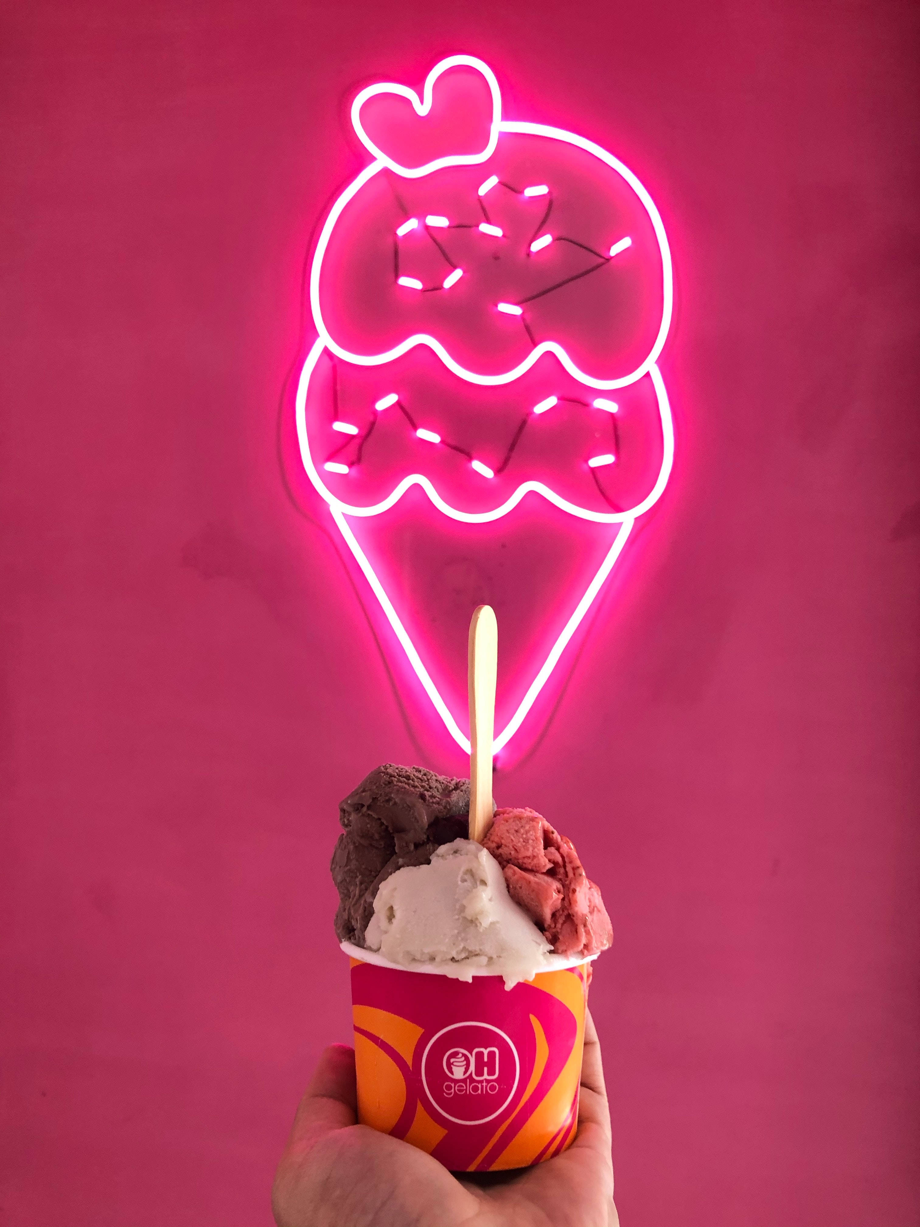 Ice Cream 桌布 壁紙 — 一隻手拿著一杯三味義式冰淇淋，在發光的粉紅色霓虹燈冰淇淋招牌下，背景是洋紅色牆壁。