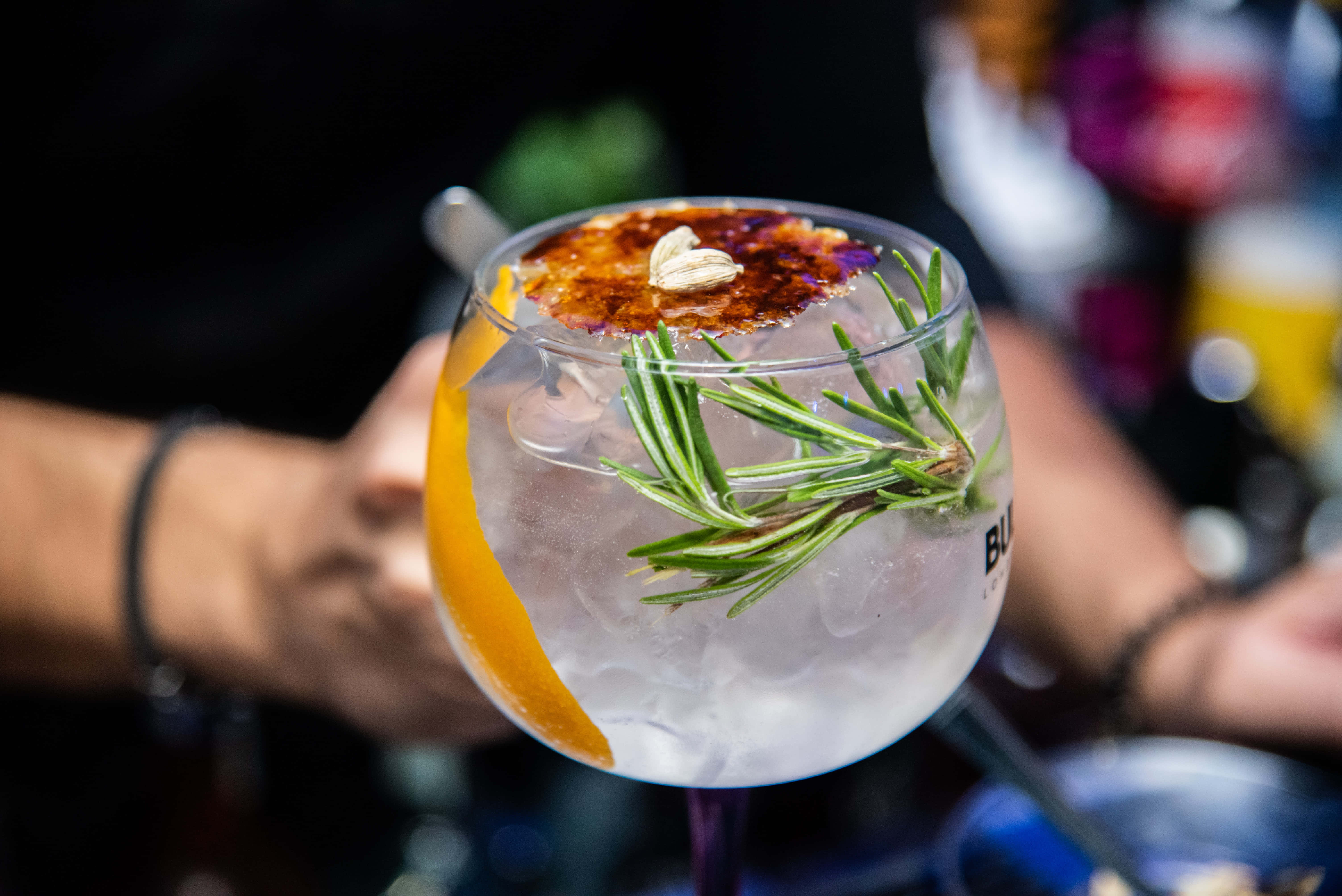 Summer Drinks 桌布 壁紙 — 一隻手拿著一杯冰涼的琴酒雞尾酒，飾以迷迭香橙片和焦糖。