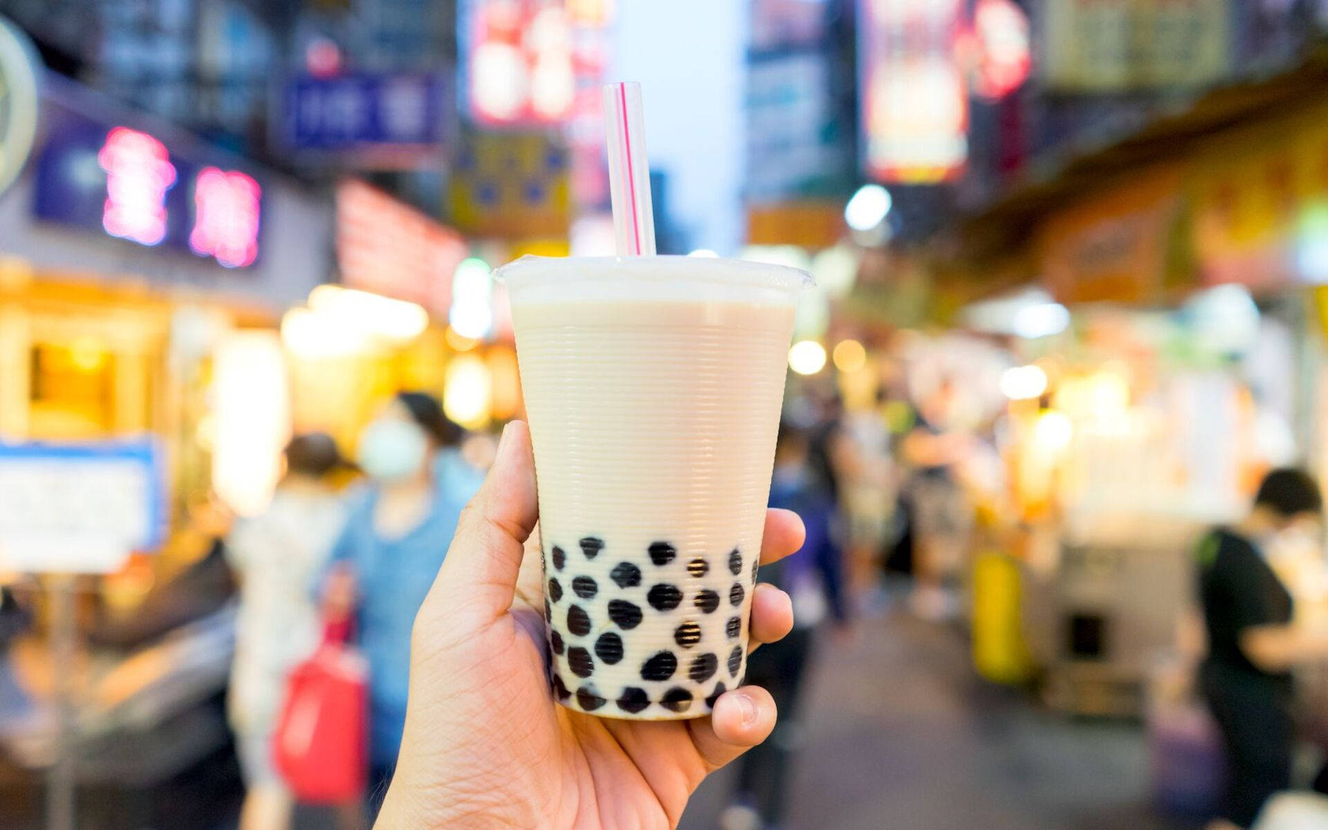 Bubble 桌布 壁紙 — 一隻手拿著一杯帶有黑珍珠的奶油珍珠奶茶，背景是充滿活力的霓虹燈夜市。