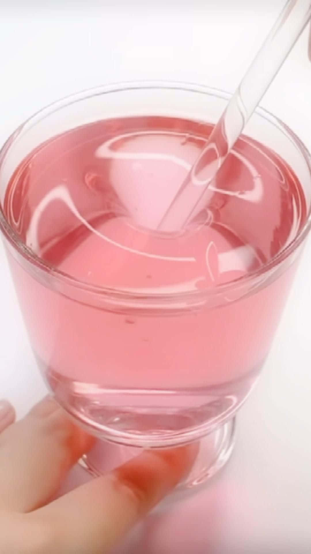 slime 桌布 壁紙 — 一隻手拿著一杯粉紅色液體，配透明吸管，在白色背景上泛起漣漪。