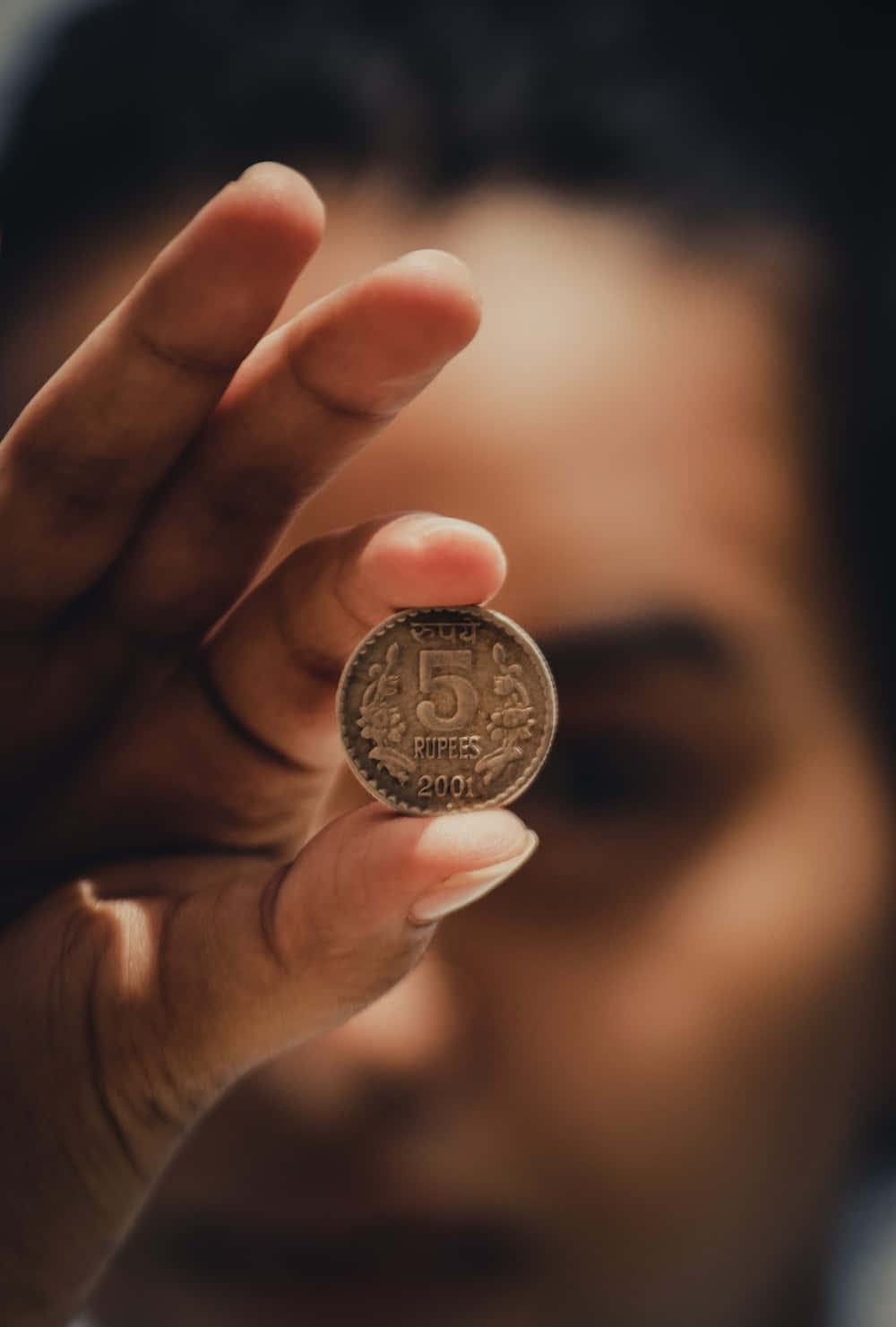 Woman 桌布 壁紙 — 一隻手拿著一枚2001年的5盧比印度硬幣，對焦清晰，背景是一張柔和模糊的人臉。