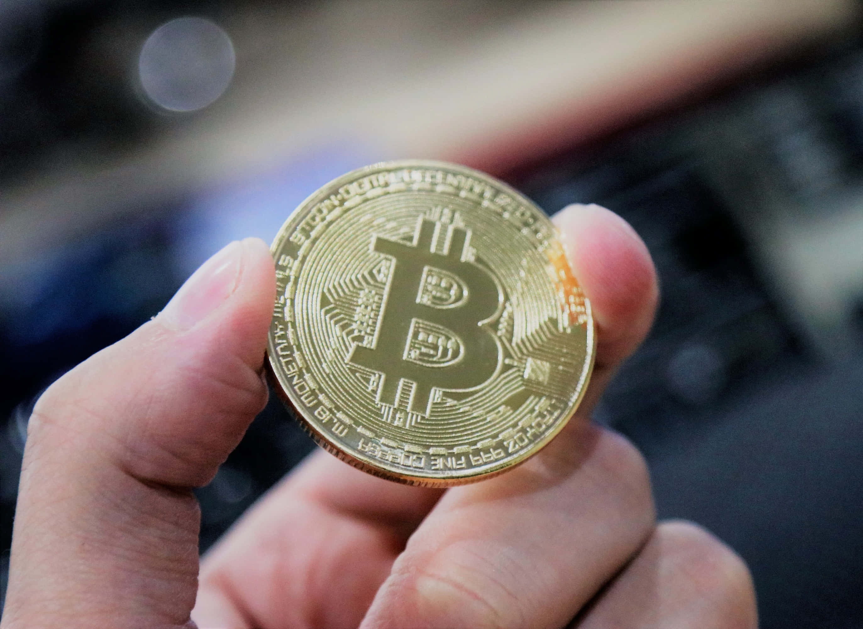 比特幣 桌布 壁紙 — 一隻手拿著一枚閃閃發光的金色比特幣硬幣，上面有電路圖案，背景是模糊的科技背景。