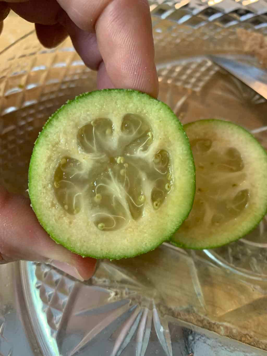 glass 桌布 壁紙 — 一隻手拿著一片切開的綠色萊姆，露出多汁的分瓣內部，放在有圖案的玻璃盤上。