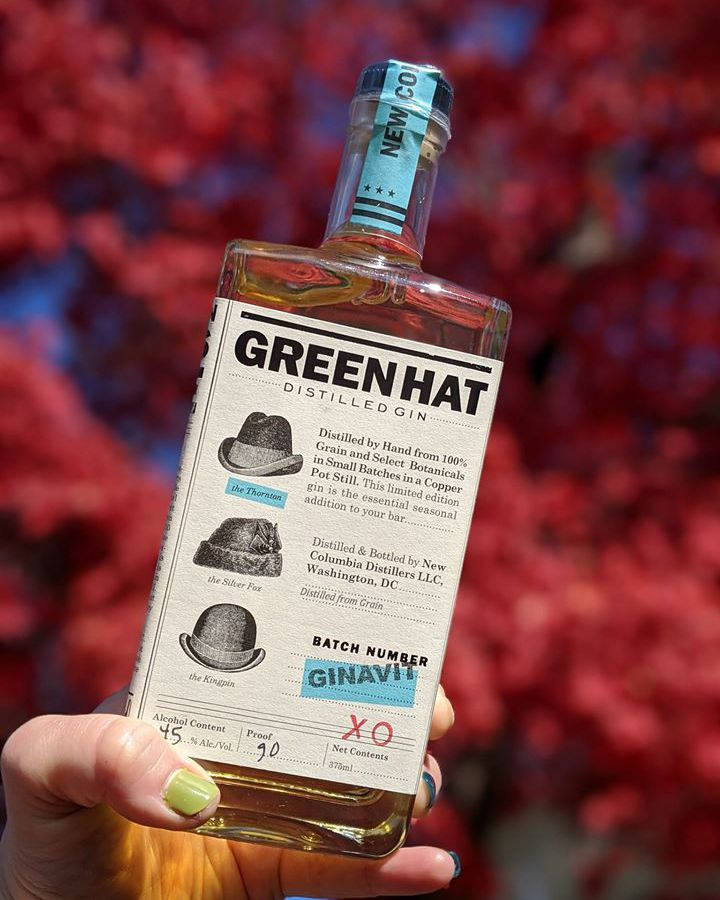 Gin 桌布 壁紙 — 一隻手拿著一瓶Green Hat Distilled Gin，背景是鮮豔的紅色和藍色模糊樹葉。