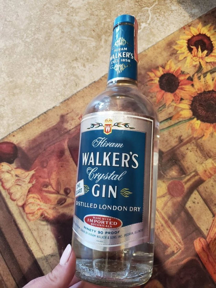 alcohol 桌布 壁紙 — 一隻手拿著一瓶透明的 Hiram Walker's Crystal Gin 琴酒，背景是向日葵圖案。