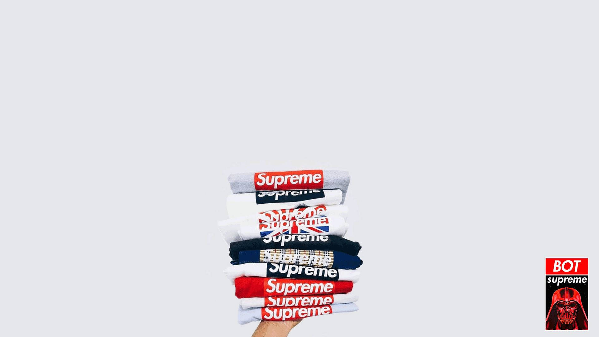 supreme 桌布 壁紙 — 一隻手拿著一疊Supreme品牌T恤，背景是純淺灰色，角落有一個小小的Darth Vader標誌。
