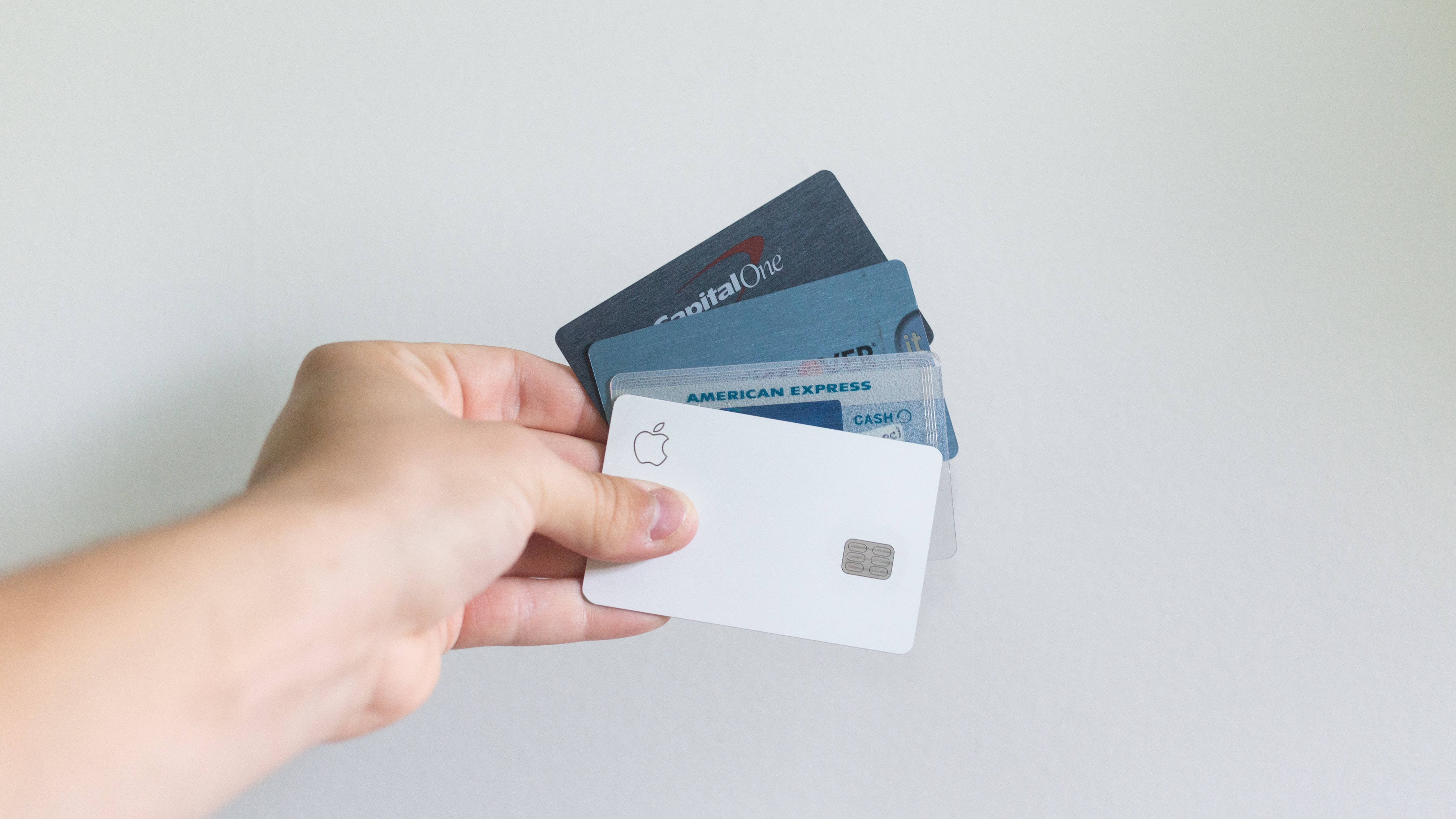 標誌 桌布 壁紙 — 一隻手拿著一疊信用卡，包括Apple Card、Capital One和American Express，背景為純白色。