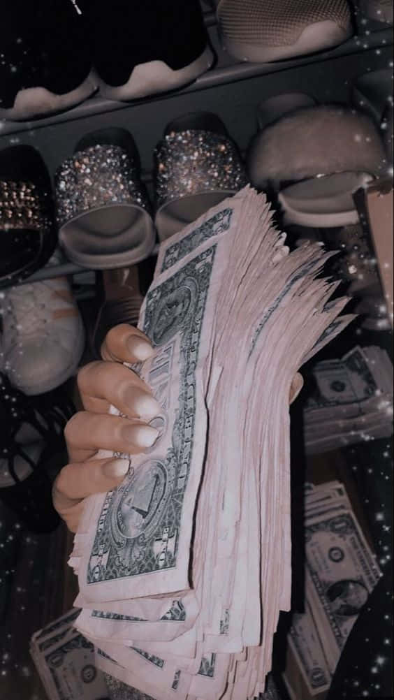 Girly Money 桌布 壁紙 — 一隻手拿著一疊厚厚的美元鈔票，背景是閃亮的鞋子和散落的現金，在星光濾鏡下。