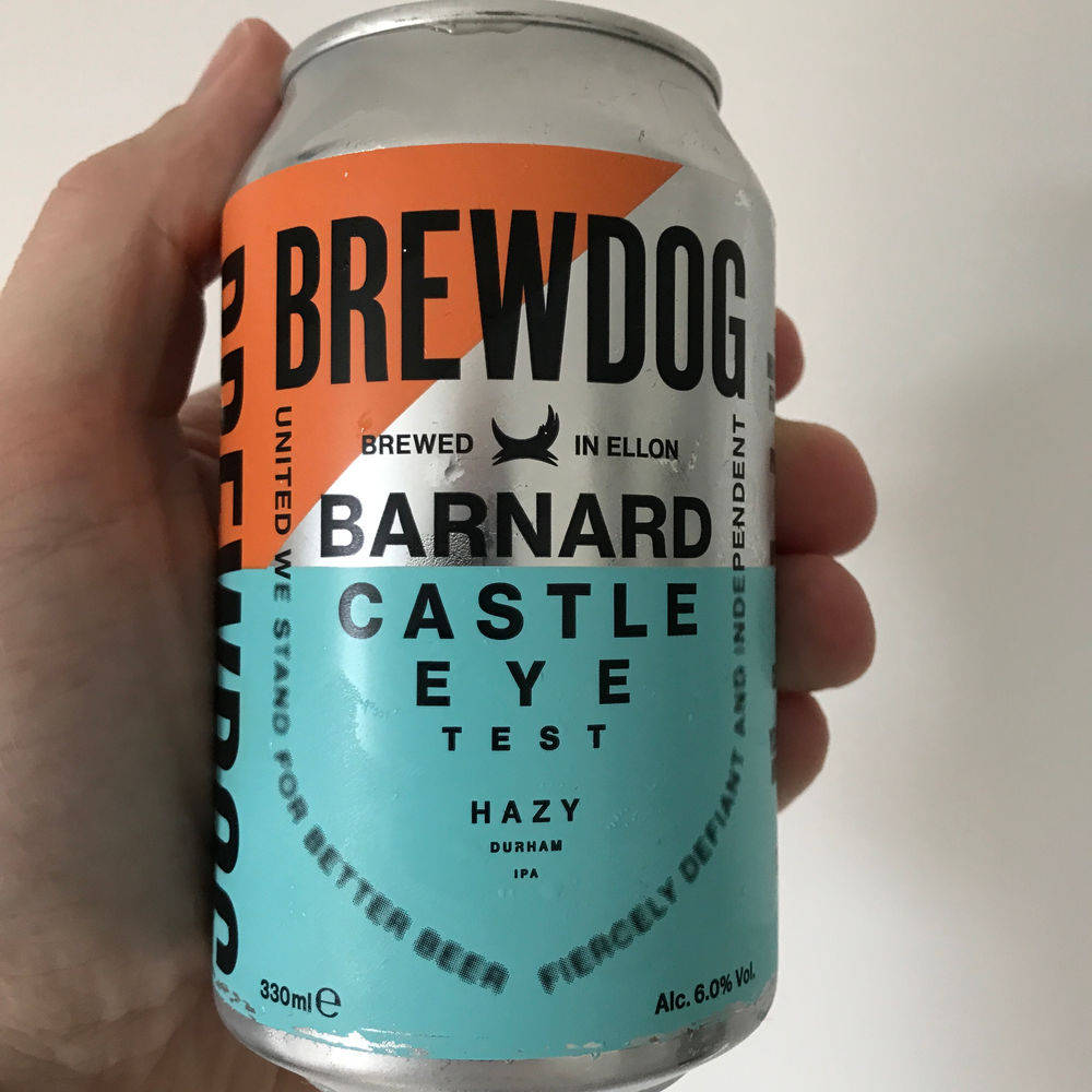 Drink 桌布 壁紙 — 一隻手拿著一罐 BrewDog Barnard Castle Eye Test hazy IPA，帶有醒目的橙色和藍綠色品牌標識，背景為純白色。