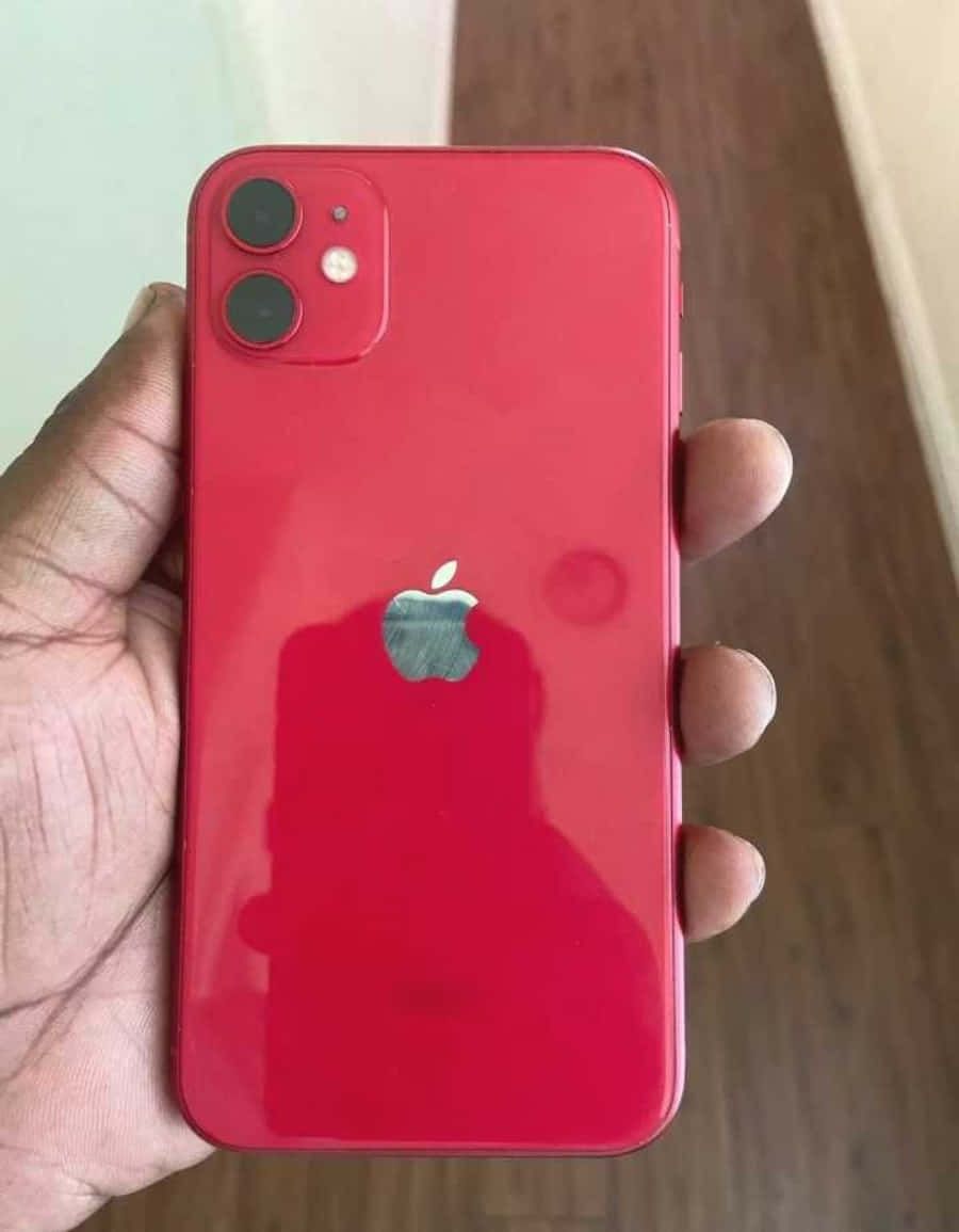 手機 桌布 壁紙 — 一隻手拿著一部亮面紅色iPhone 11，雙鏡頭和Apple標誌反射周圍環境。