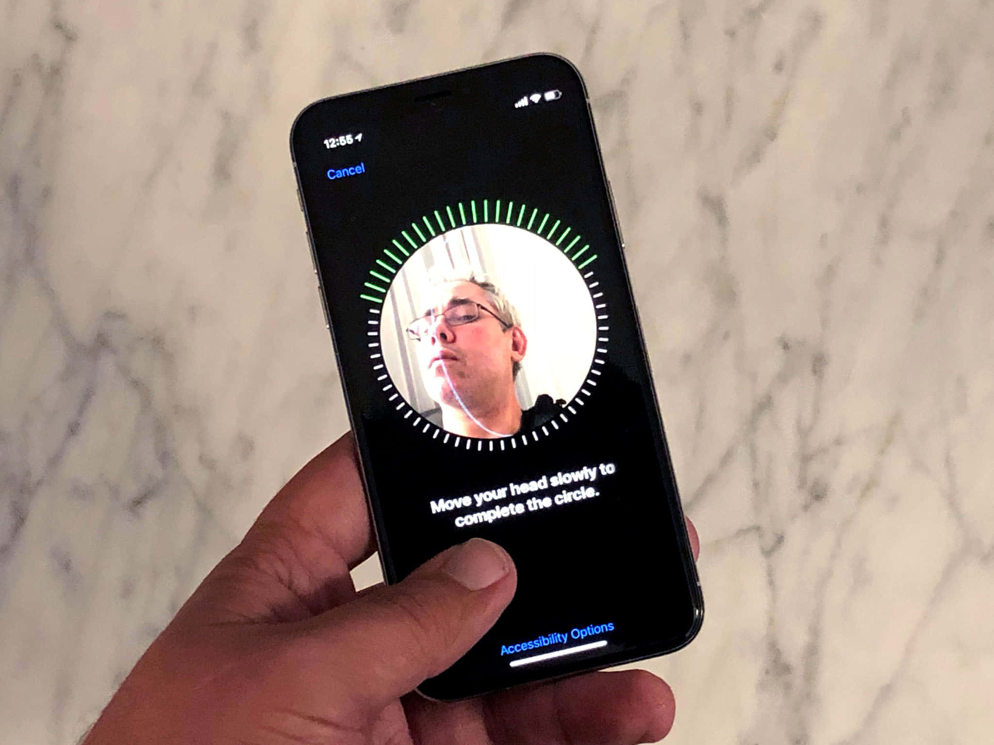 Face Id 桌布 壁紙 — 一隻手拿著一部智慧型手機，在大理石背景上顯示無障礙面部追蹤功能。