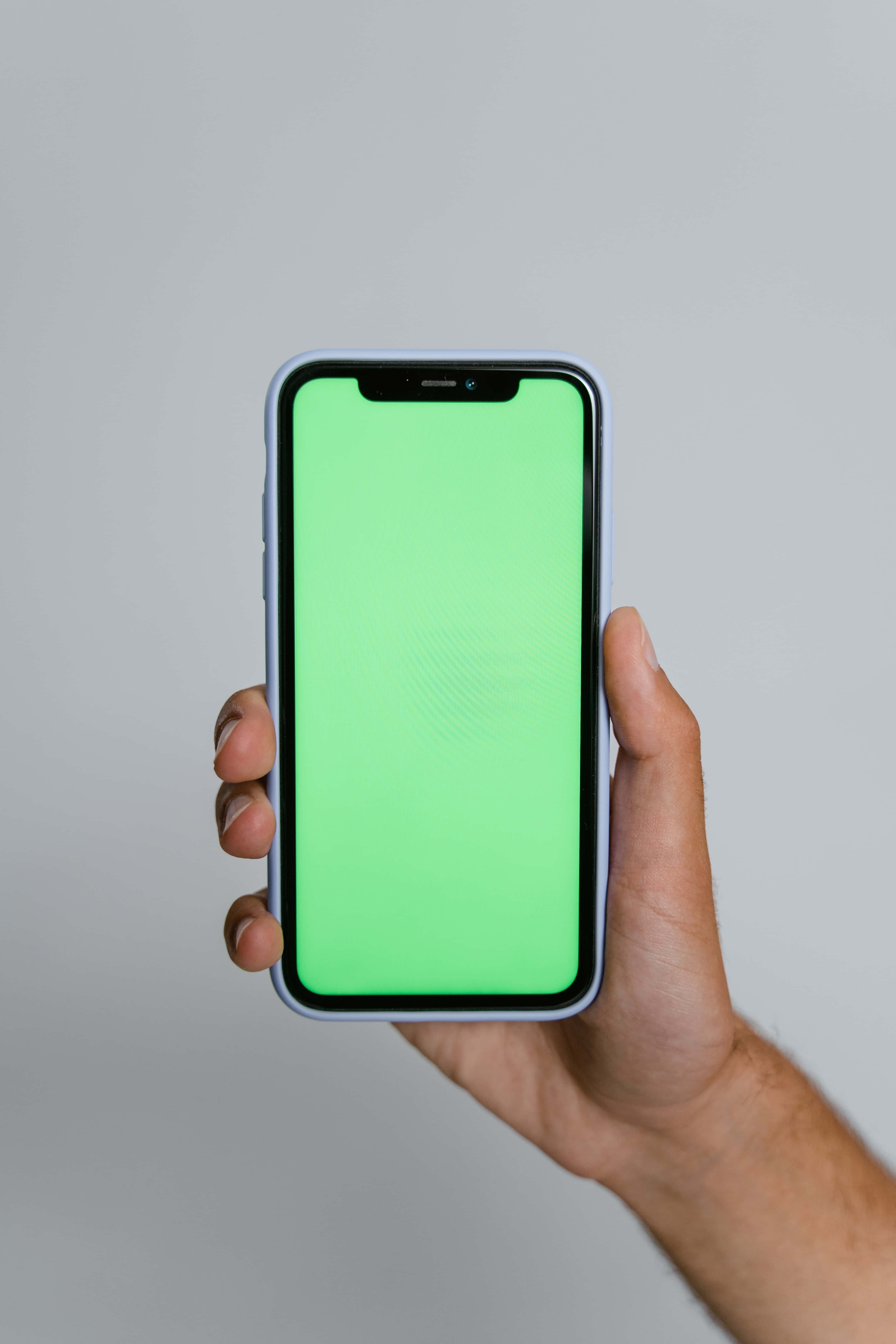 iPhone 桌布 壁紙 — 一隻手拿著一部螢幕亮綠色的智慧型手機，背景是純灰色。