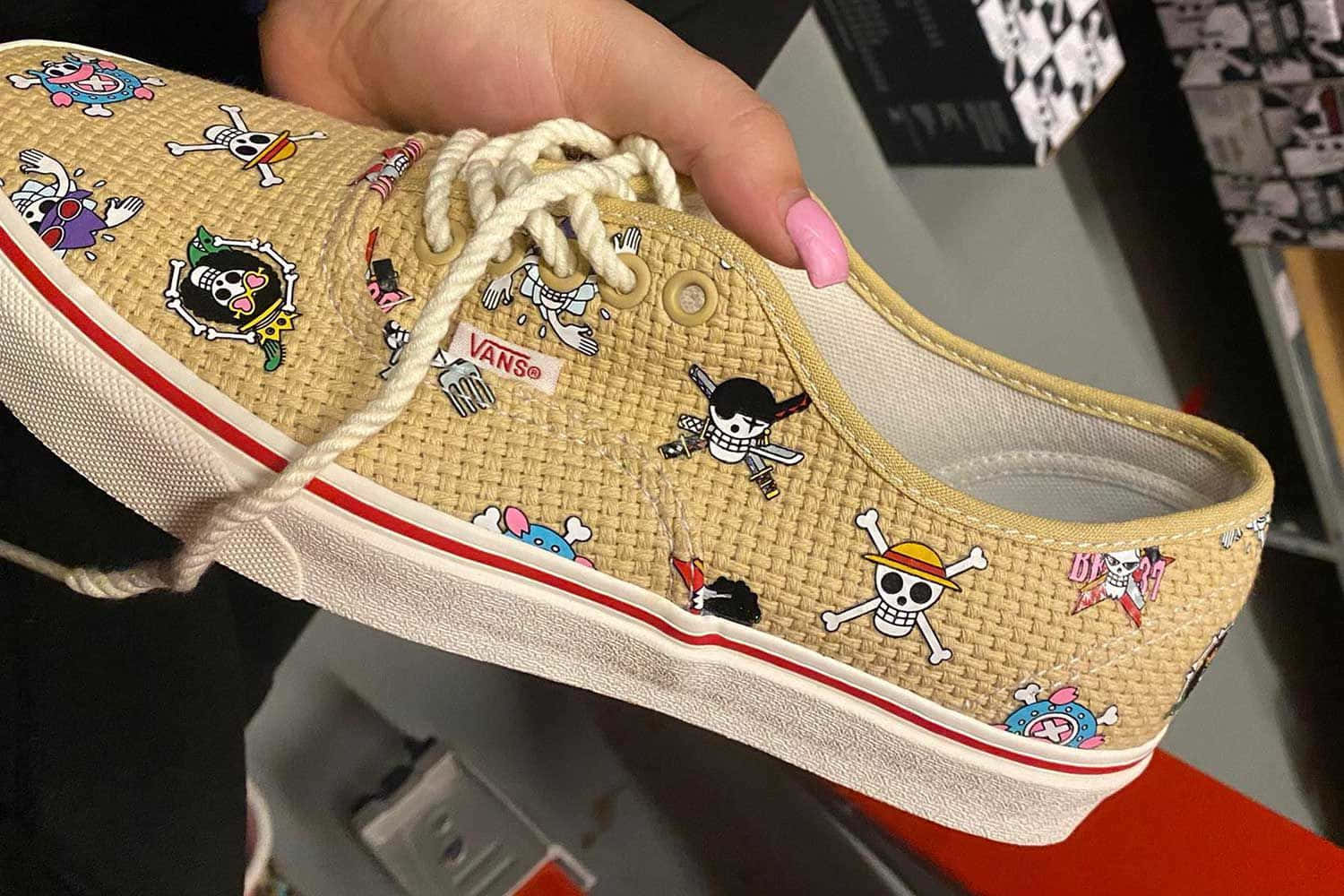 Vans 桌布 壁紙 — 一隻手拿著一雙米色Vans運動鞋，上面覆蓋著色彩繽紛的One Piece動漫角色貼片。