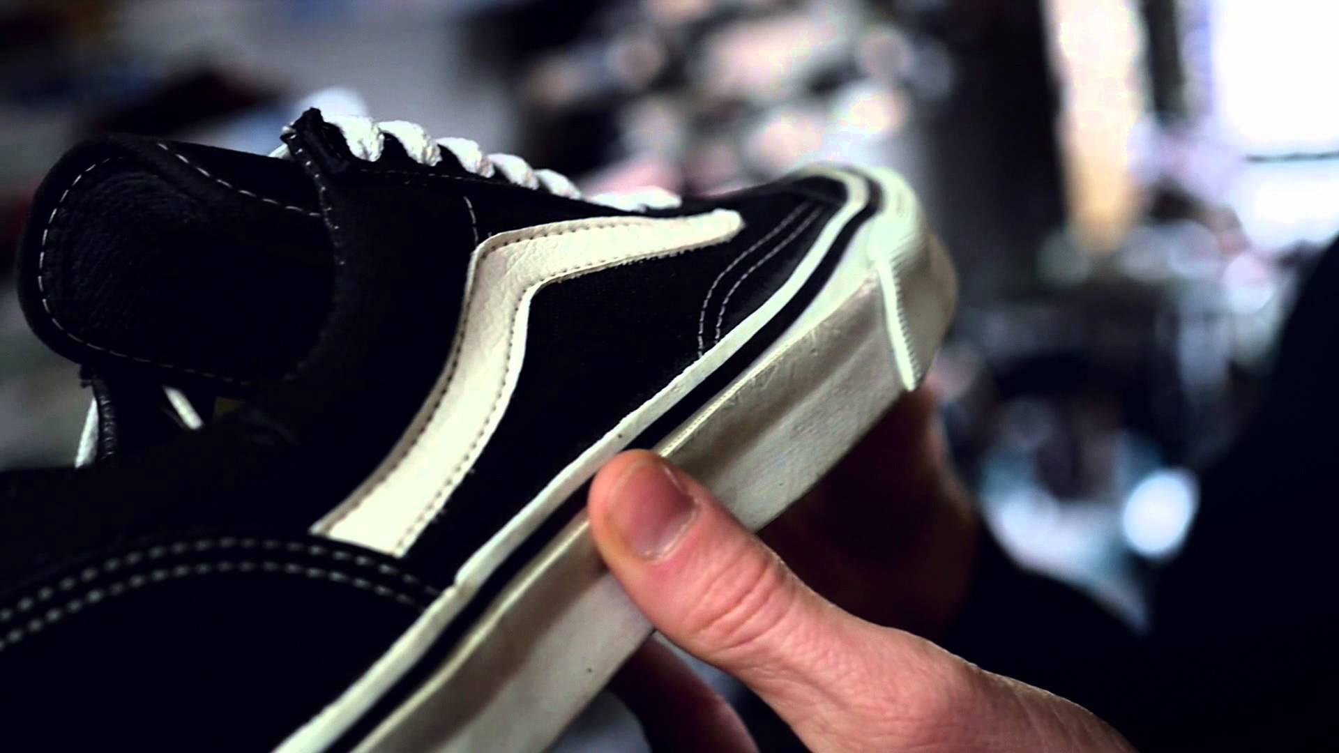 Vans Off The Wall 桌布 壁紙 — 一隻手拿著一雙黑白Vans運動鞋的特寫，可見縫線和磨損的鞋底。