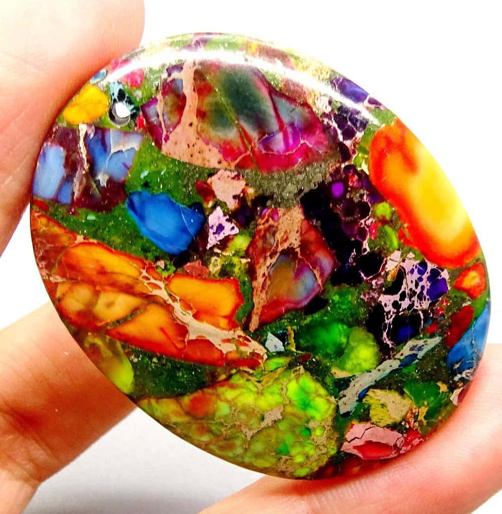 Stone 桌布 壁紙 — 一隻手拿著一顆色彩繽紛、帶有綠色、藍色、紅色和橙色漩渦圖案的拋光石。