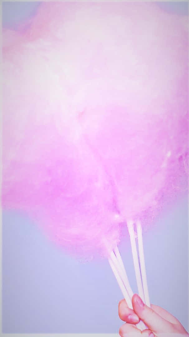 Cotton Candy 桌布 壁紙 — 一隻手拿著三個粉紅色 fluffy 棉花糖，背景是柔和的薰衣草色。