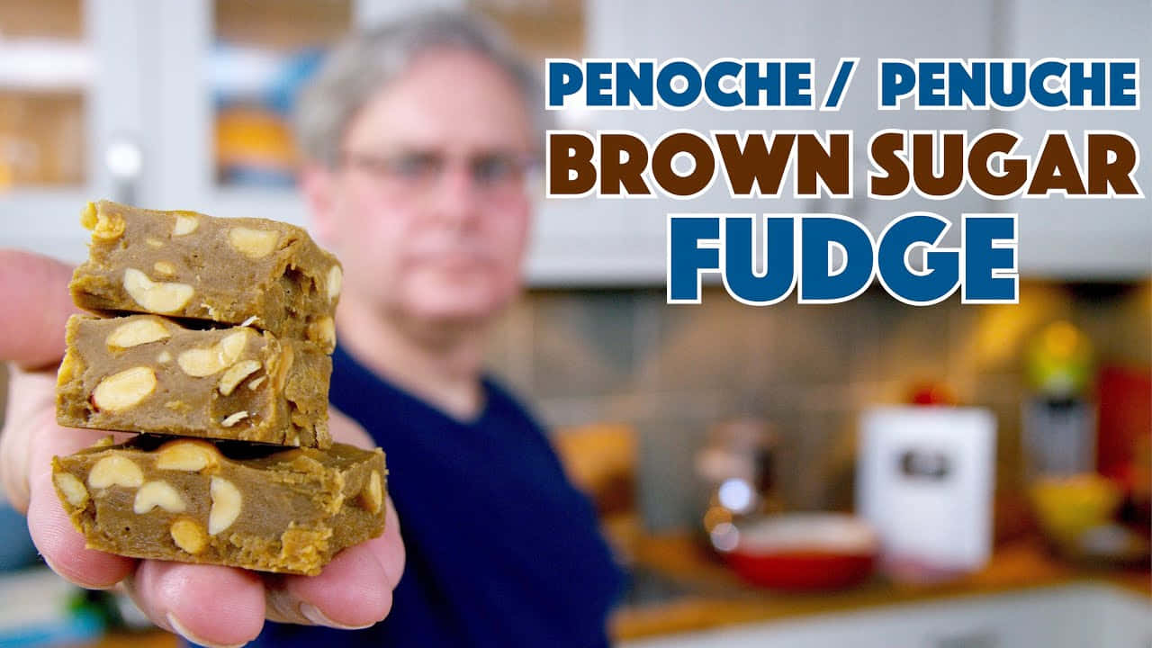 Penuche Fudge 桌布 壁紙 — 一隻手拿著三塊疊起的紅糖軟糖，上面嵌有花生，背景是模糊的廚房。