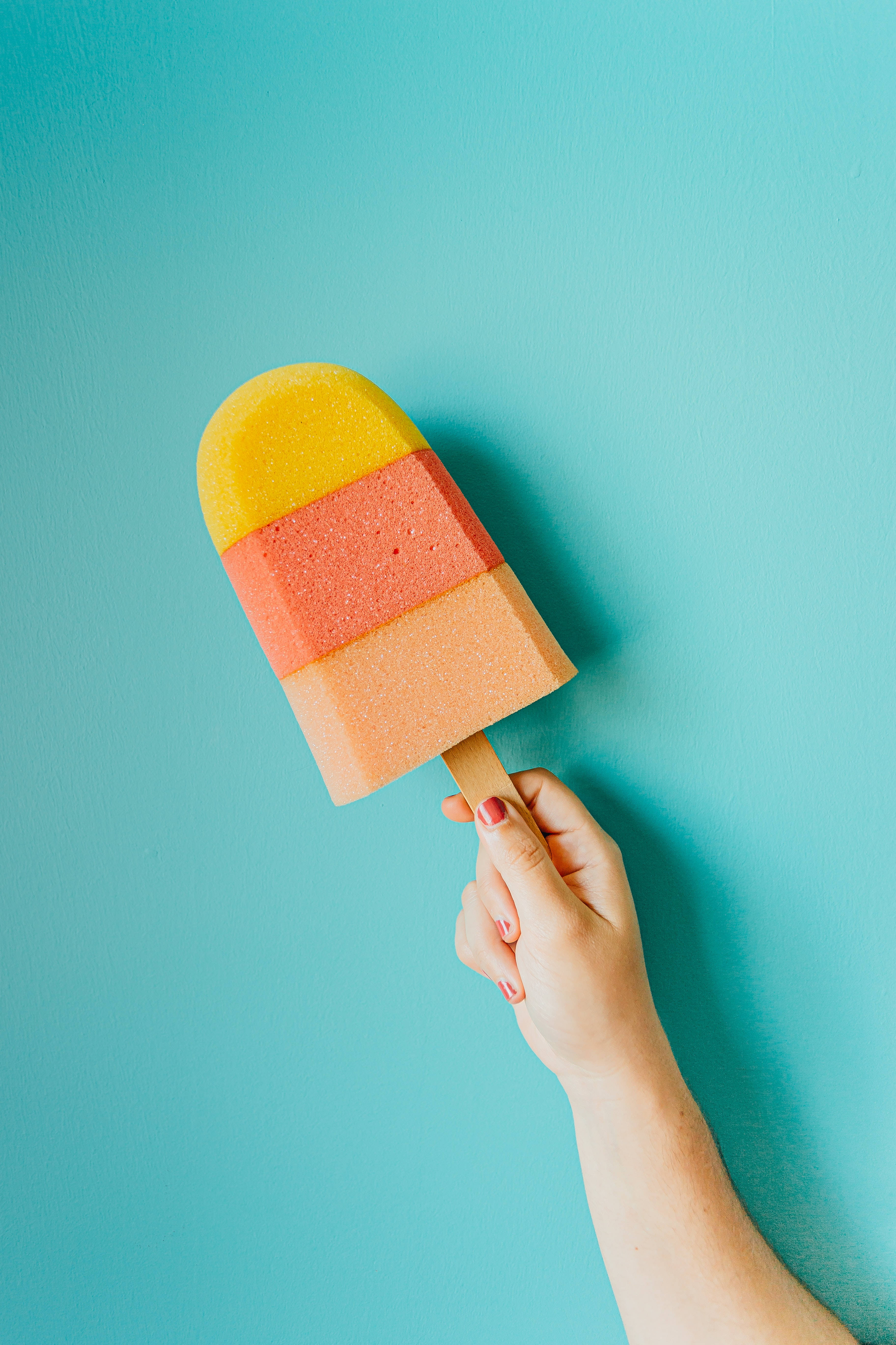 Ice Cream 桌布 壁紙 — 一隻手拿著三色冰棒，背景為純青色，展現充滿活力的夏日色彩。