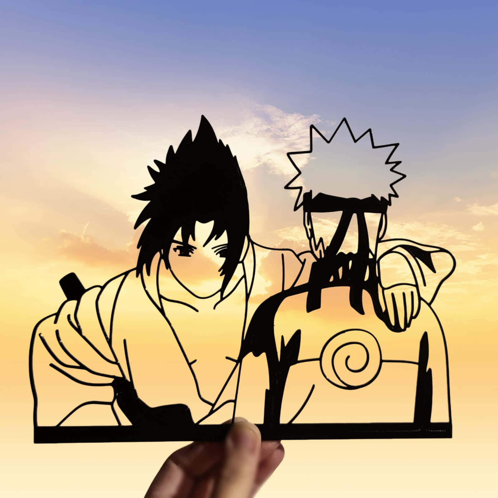 Sasuke Naruto 桌布 壁紙 — 一隻手拿著兩個動漫角色的黑色剪影剪紙，背景是溫暖的日落天空。